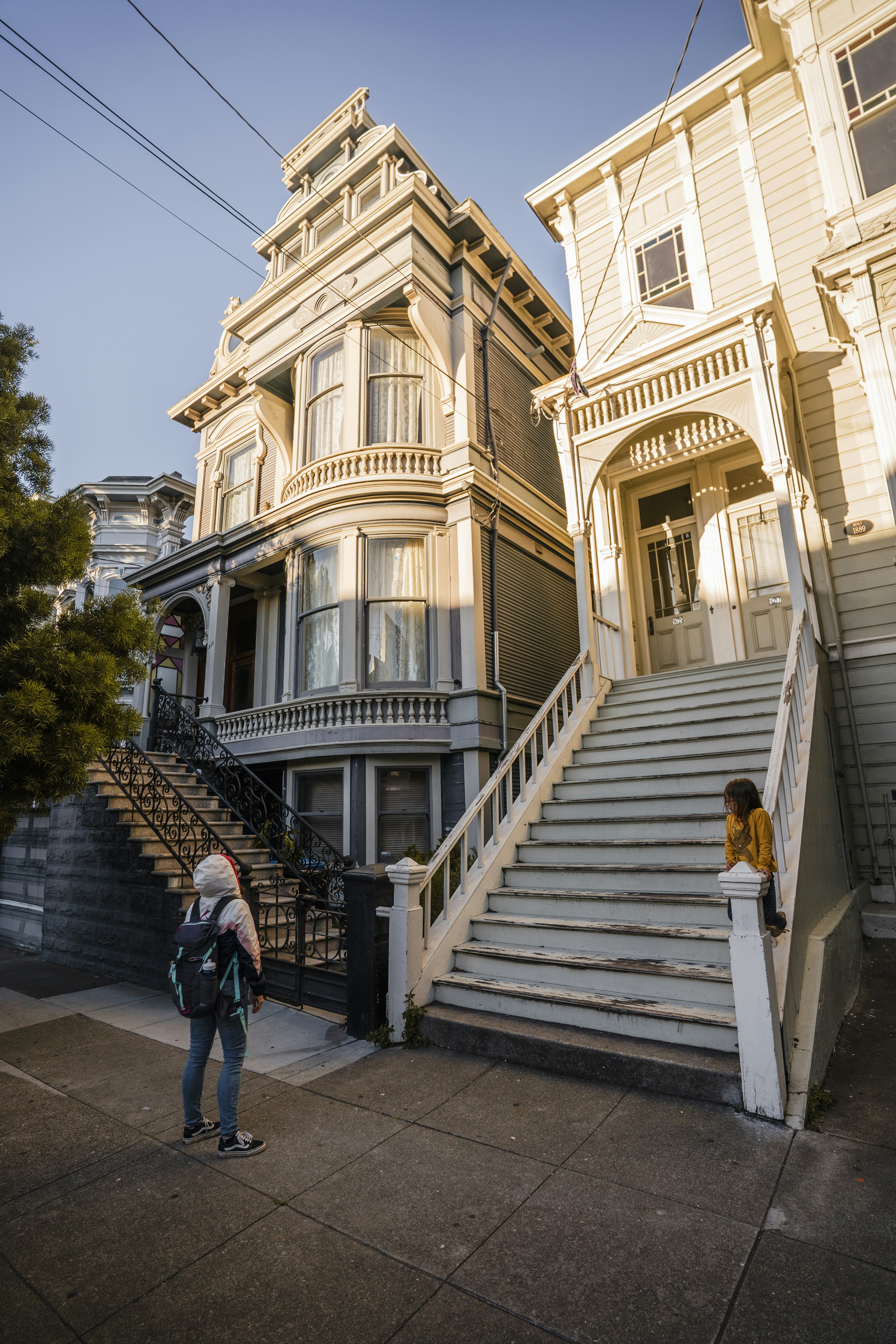Two people stand on sidewalk in front of victorian houses - free historic places to visit