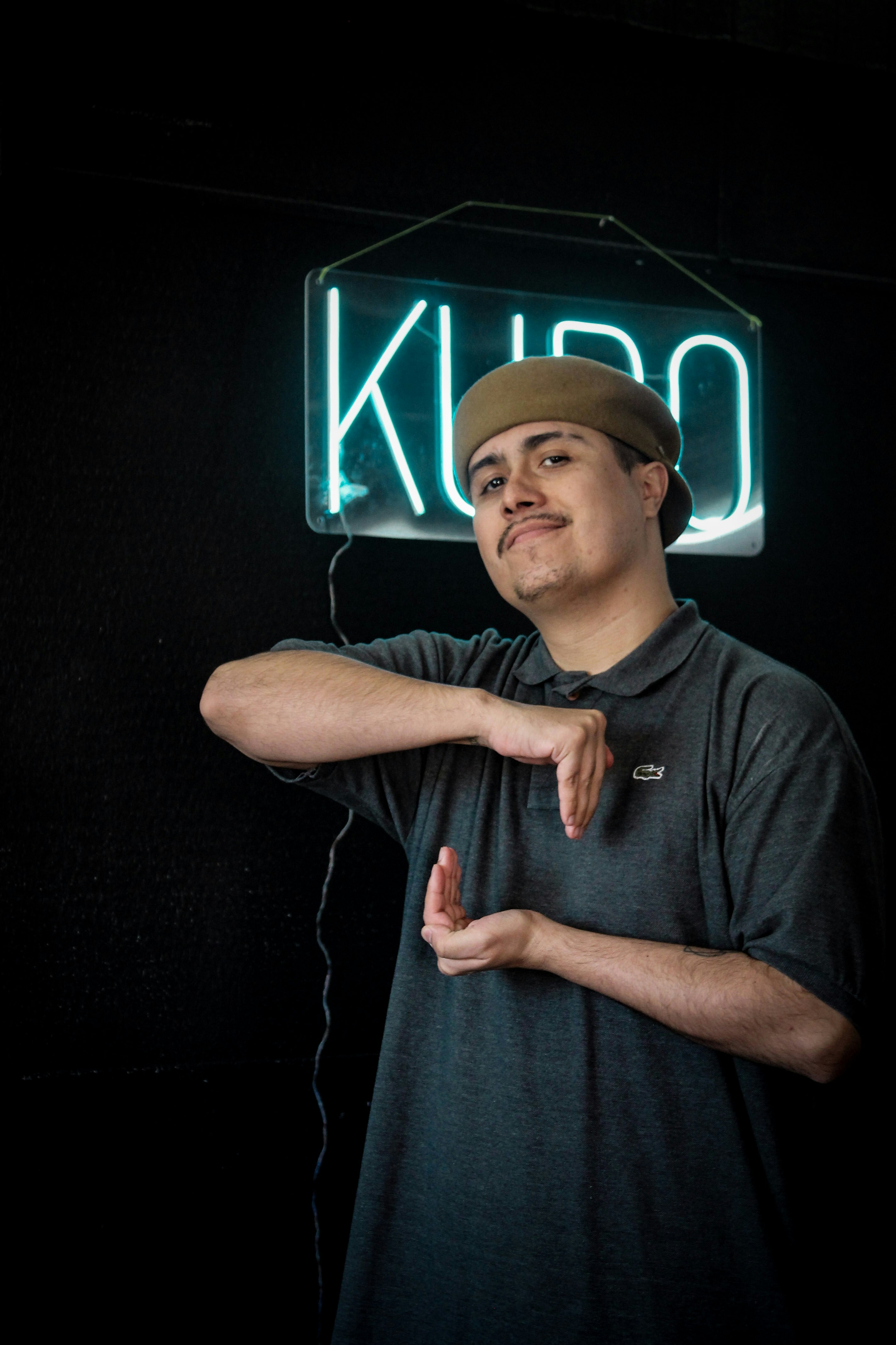 Man in hat gestures in front of neon sign