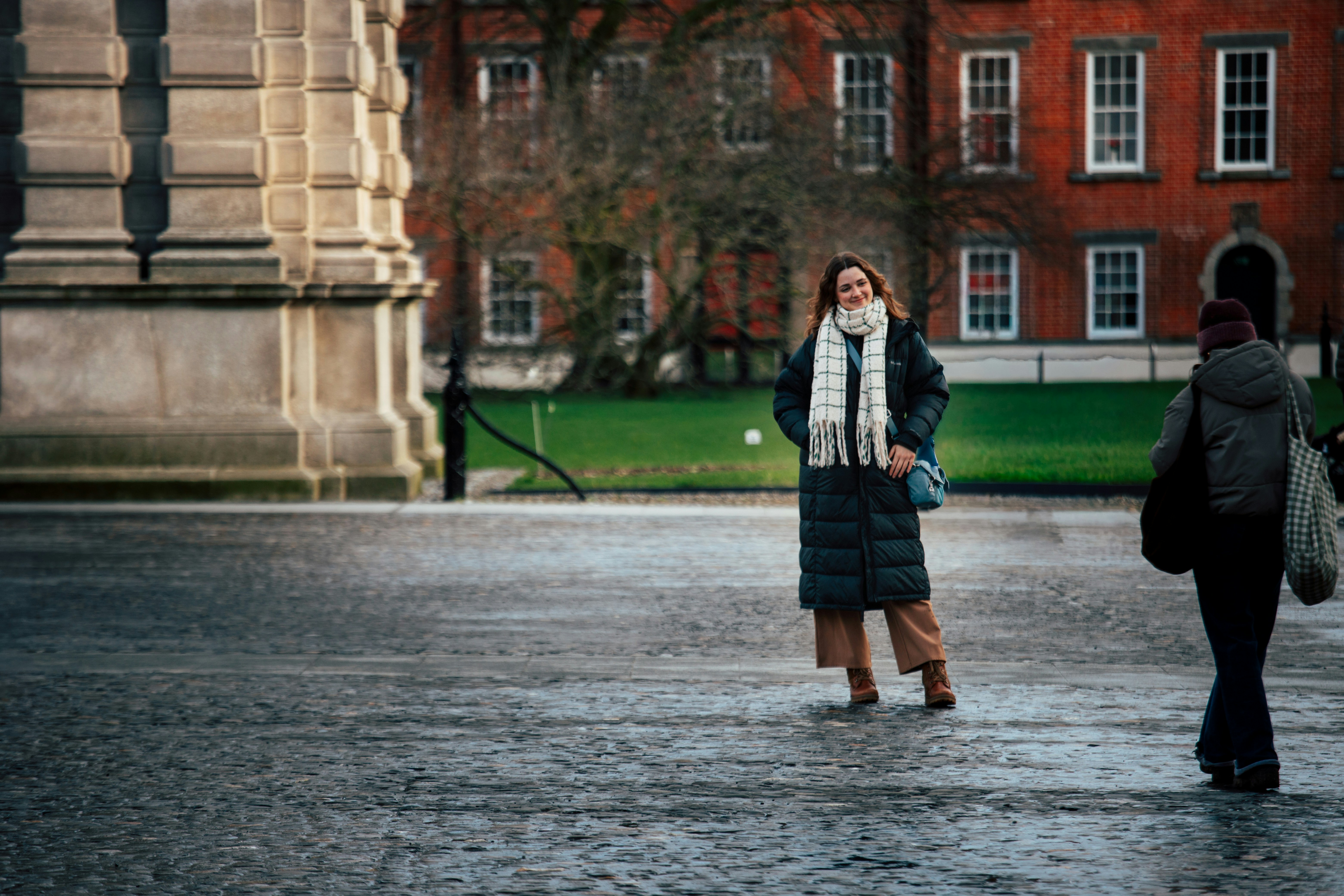 Woman in a long coat and scarf stands outside.