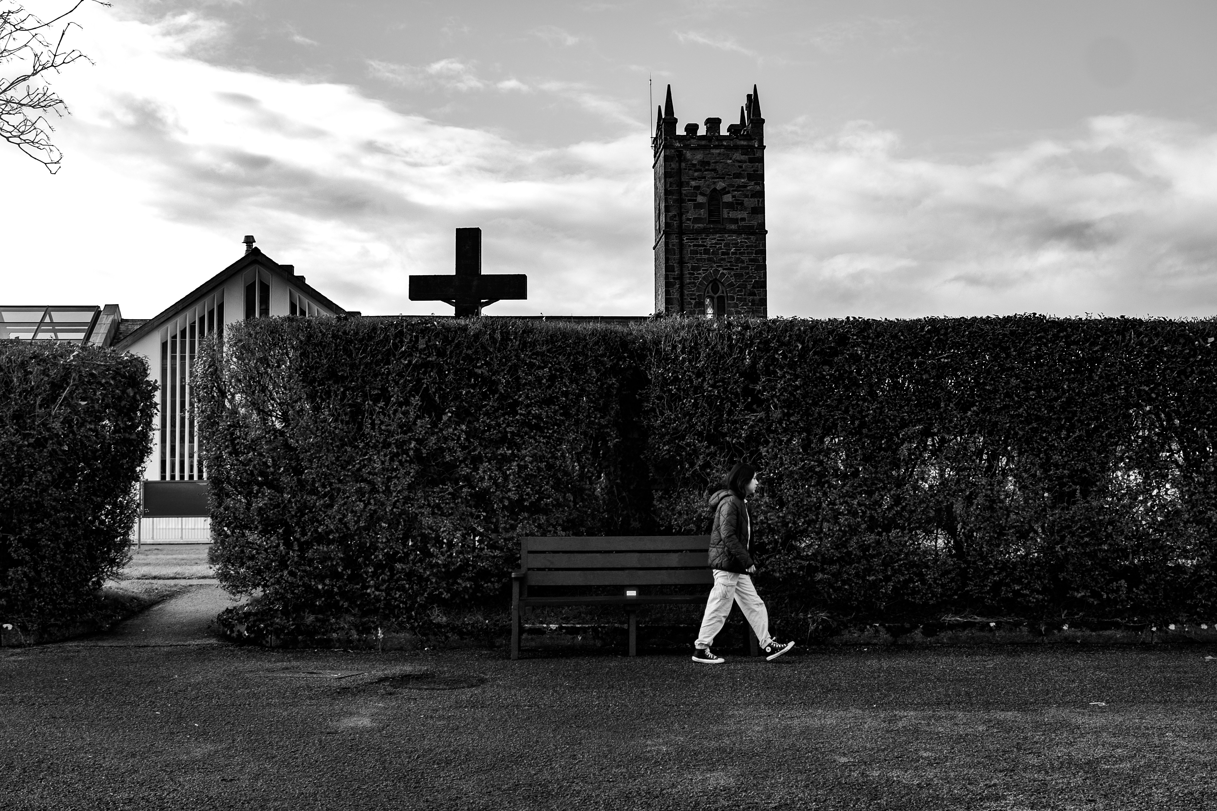 Eine Person geht an einer Hecke mit einem Kirchturm vorbei.