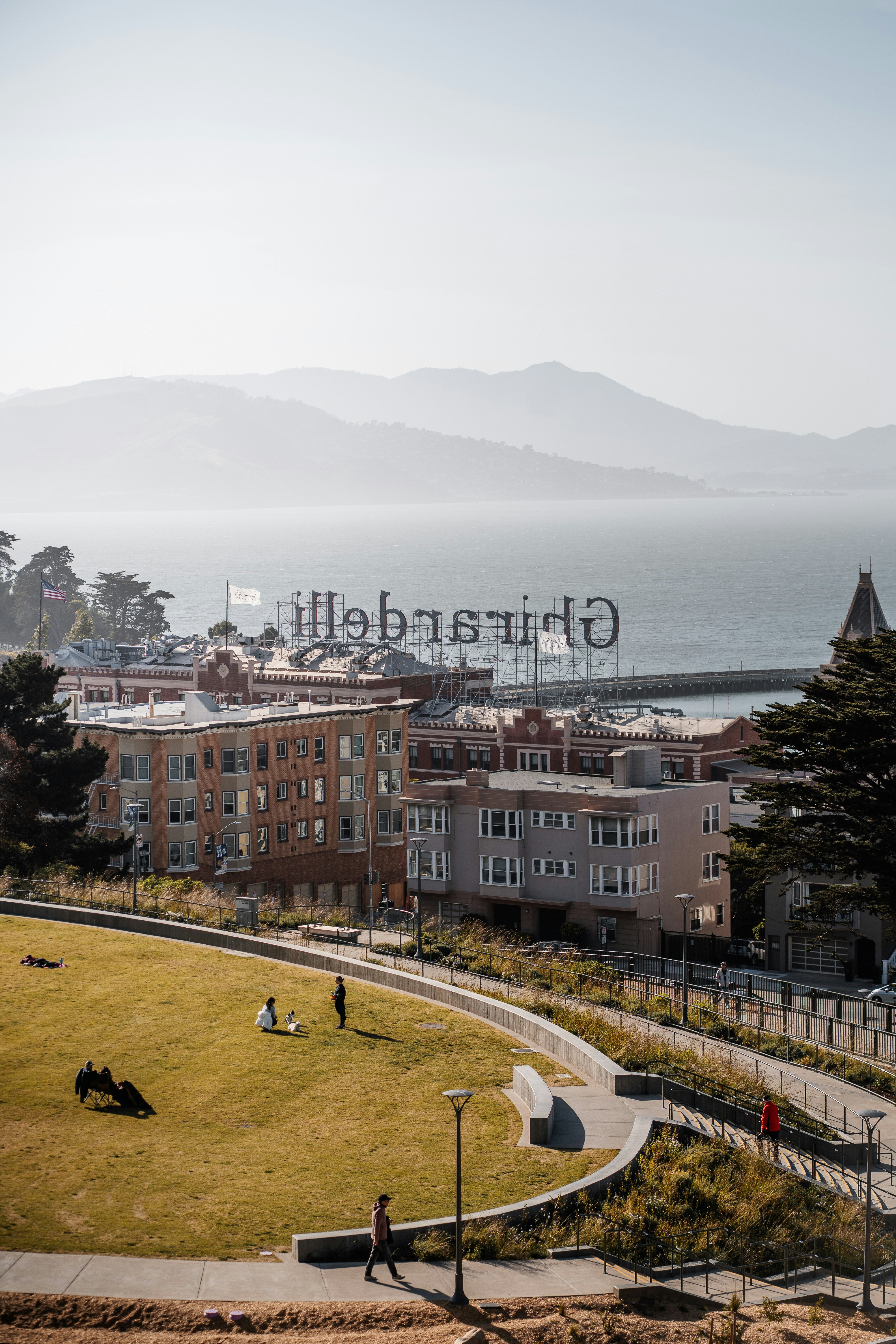 Ghirardelli sign overlooks a bay with distant mountains.