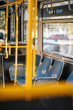 Empty bus seats with yellow poles and windows.