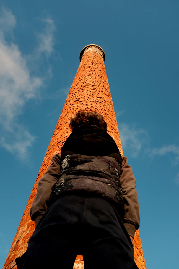 Person standing at the base of a tall brick smokestack.