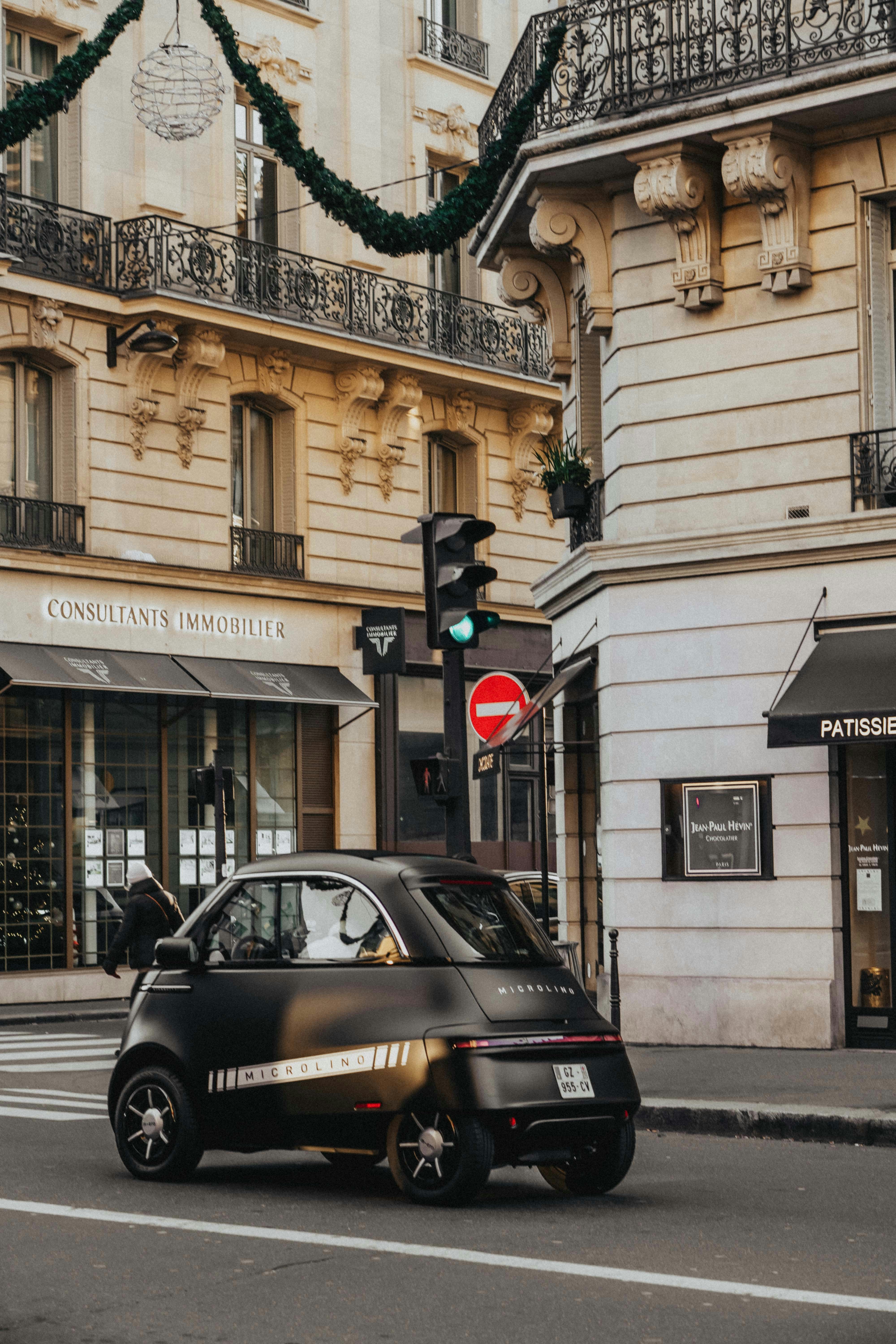 A small black car drives down a city street.