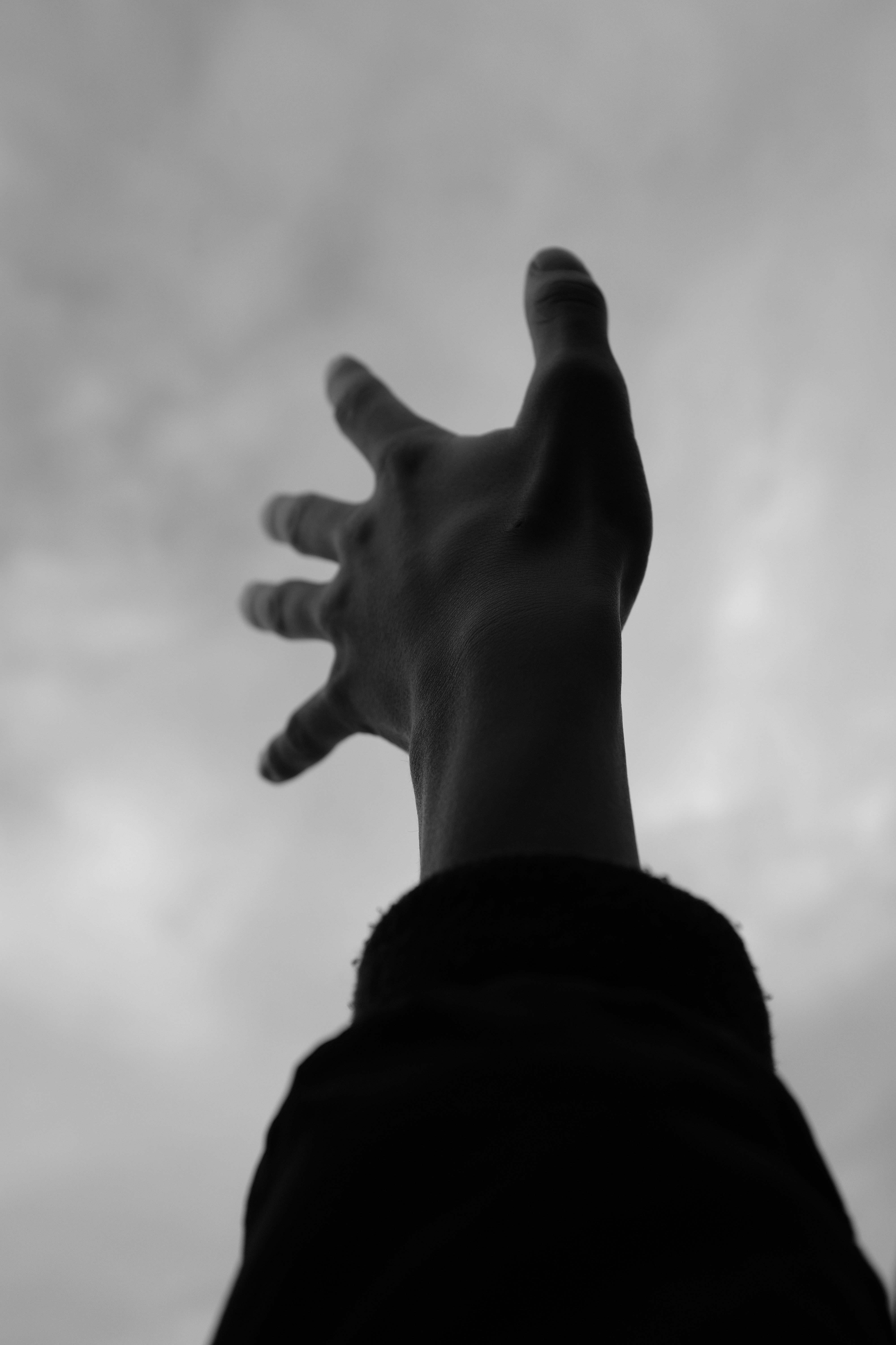 A hand reaching up towards a cloudy sky