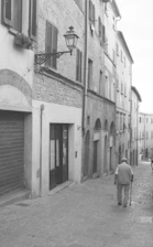 Elderly man walks down a cobblestone street with buildings.