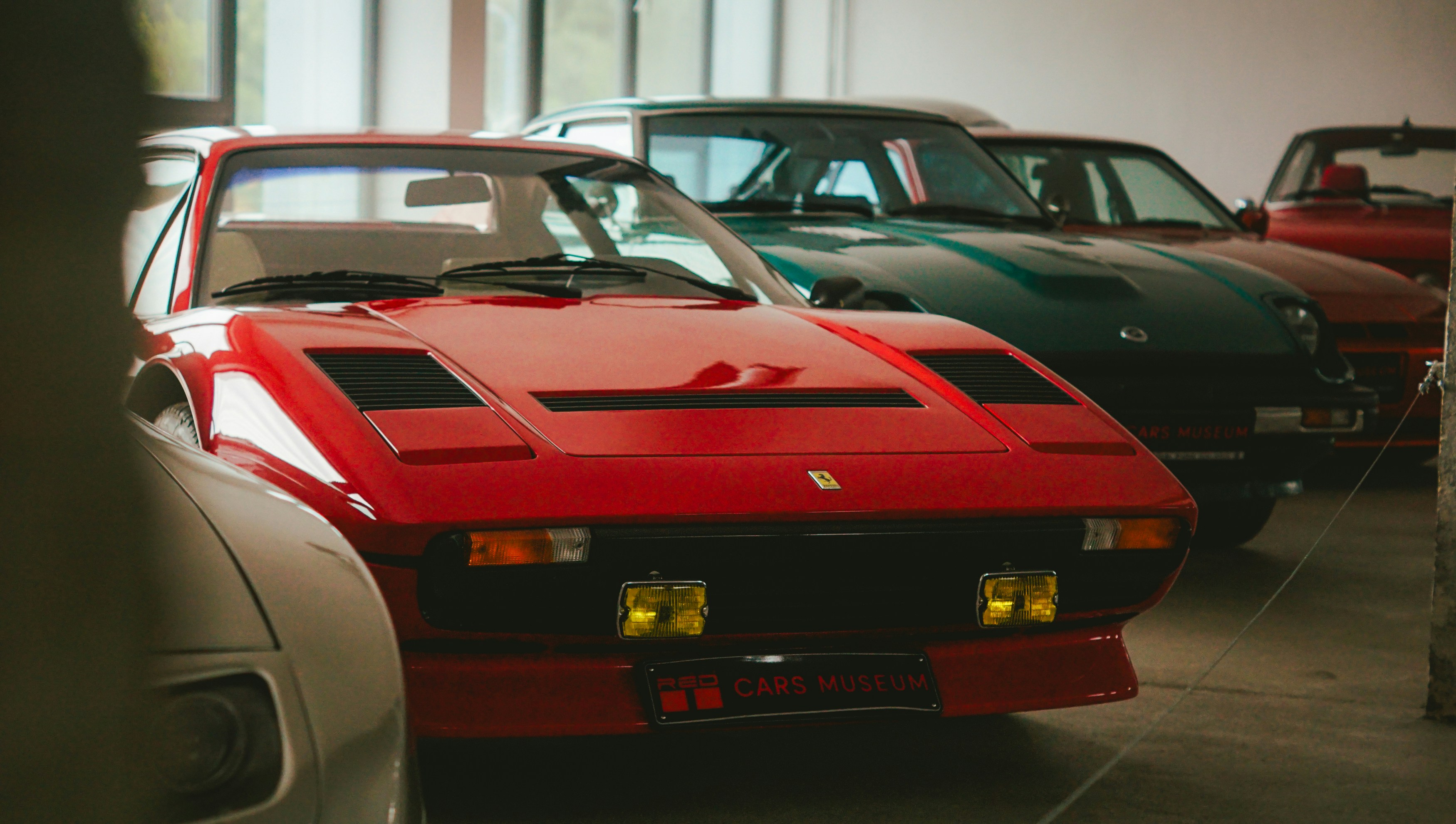 Several vintage cars parked indoors, red car in front.
