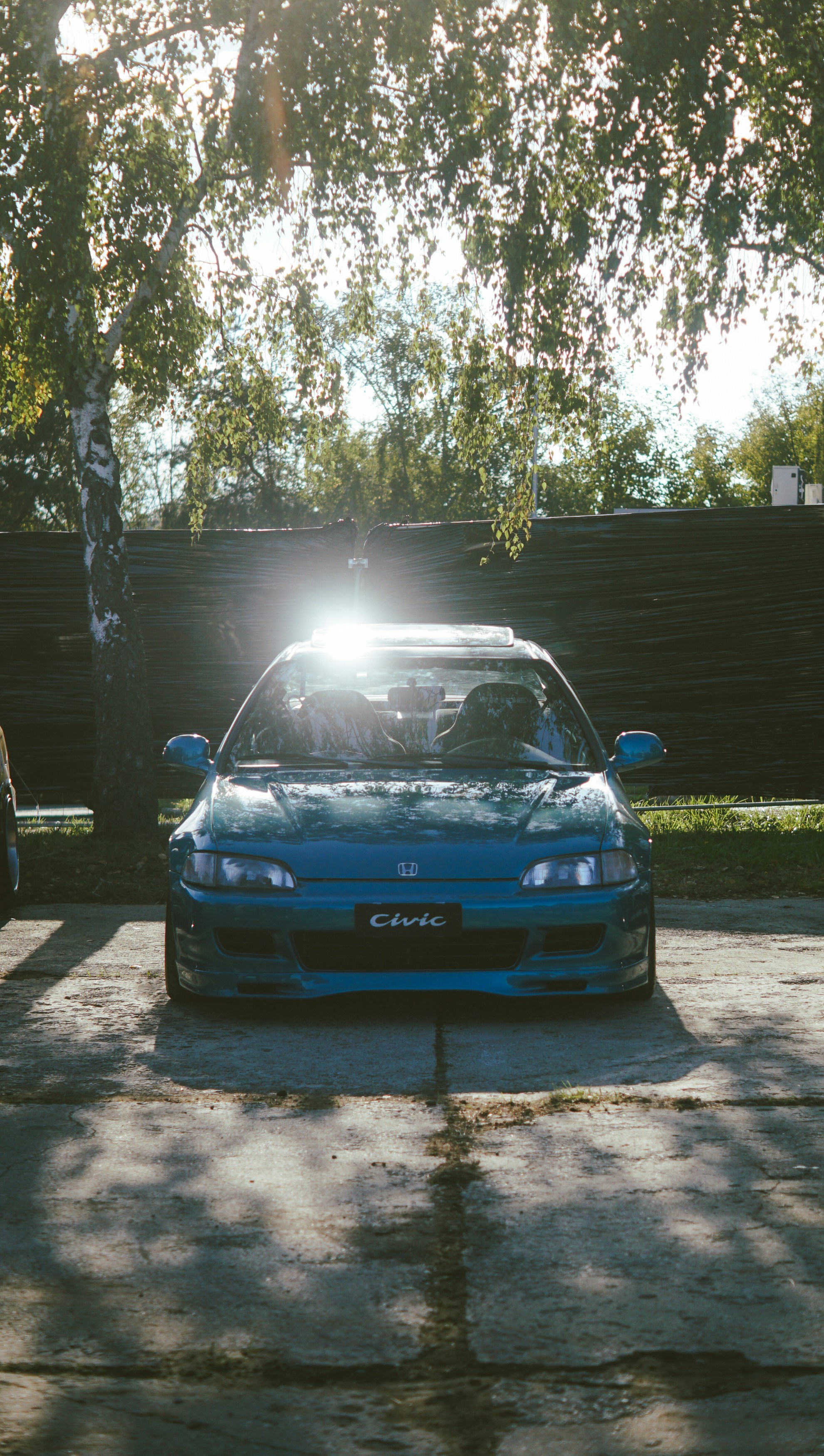 Blue honda civic parked under trees with sun flare