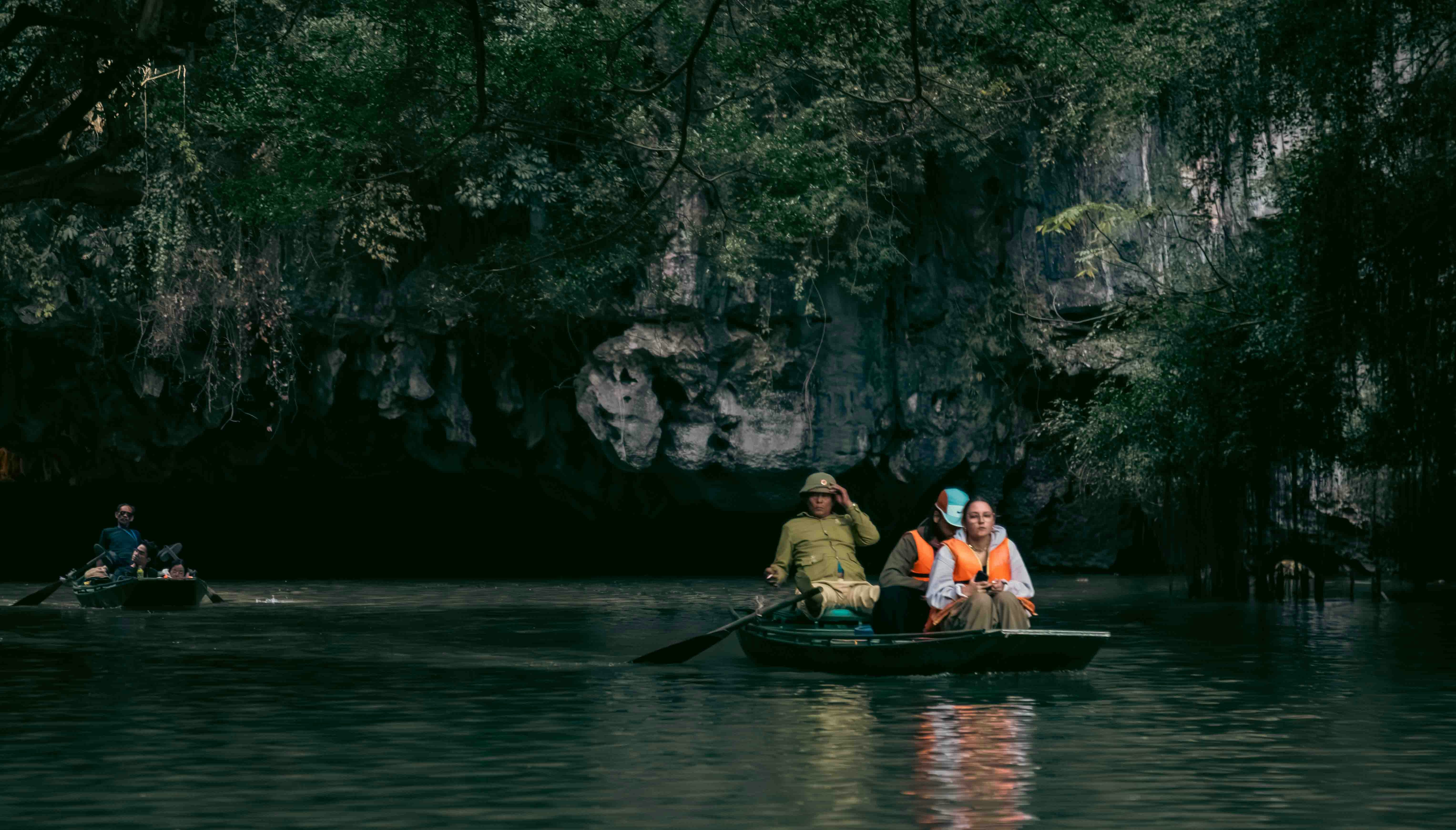 People rowing boats in a lush, rocky river landscape.