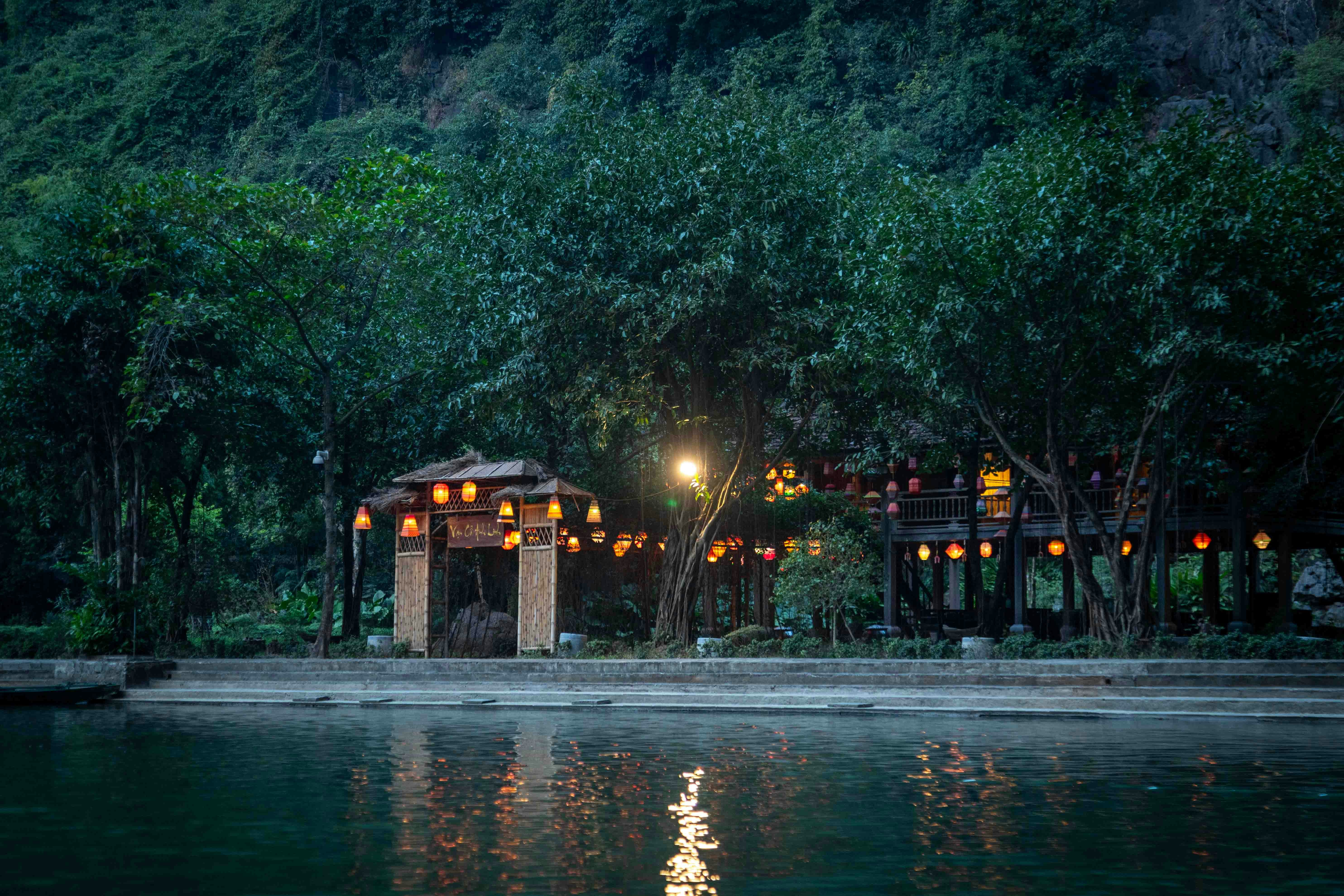 Lanterns illuminate a tranquil waterside pavilion at dusk.