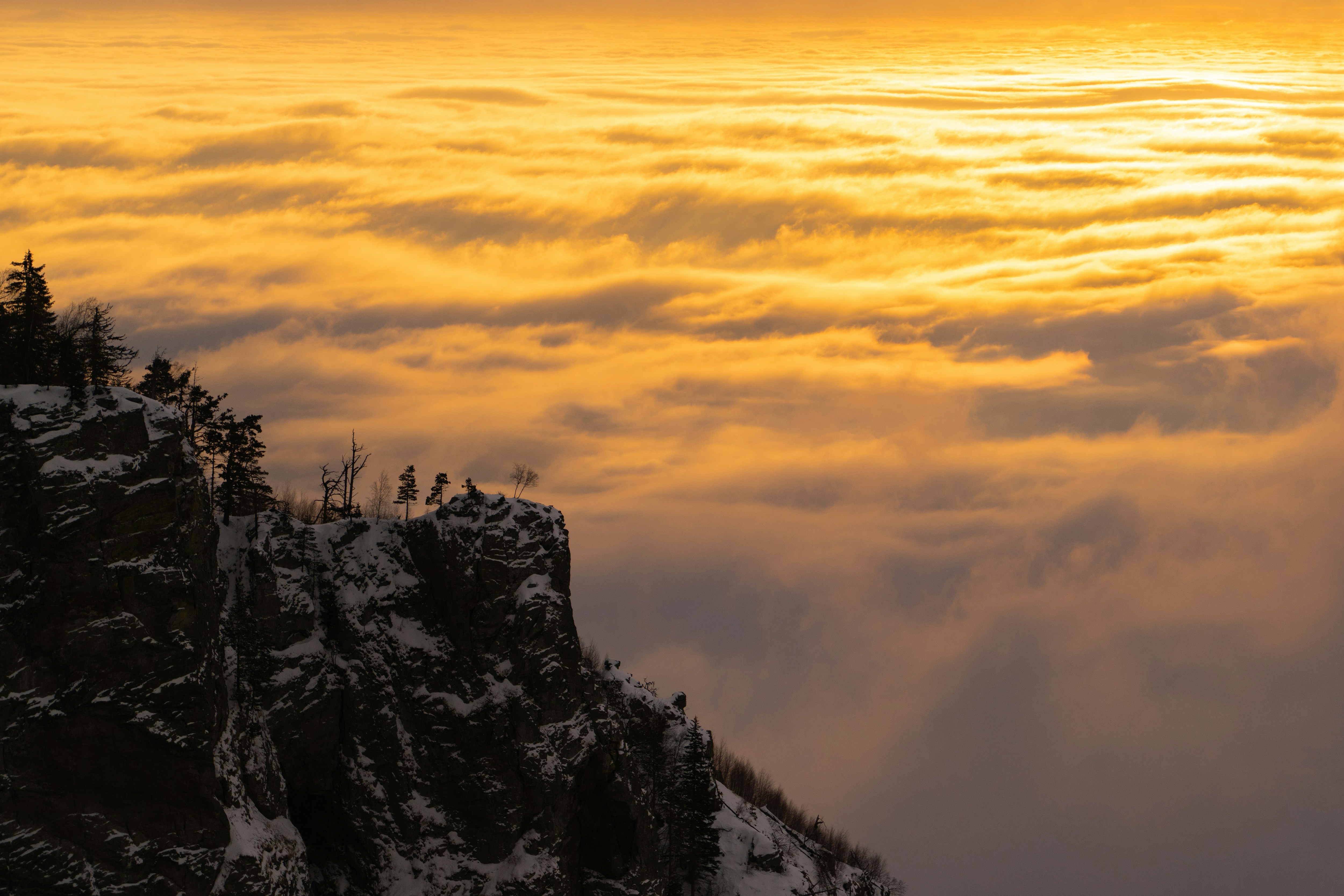 Snowy mountain peak above golden clouds at sunrise