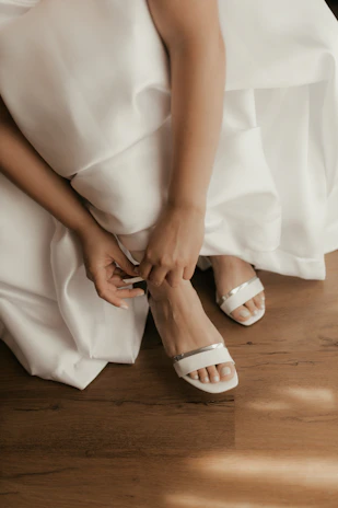 Bride putting on white sandals before wedding