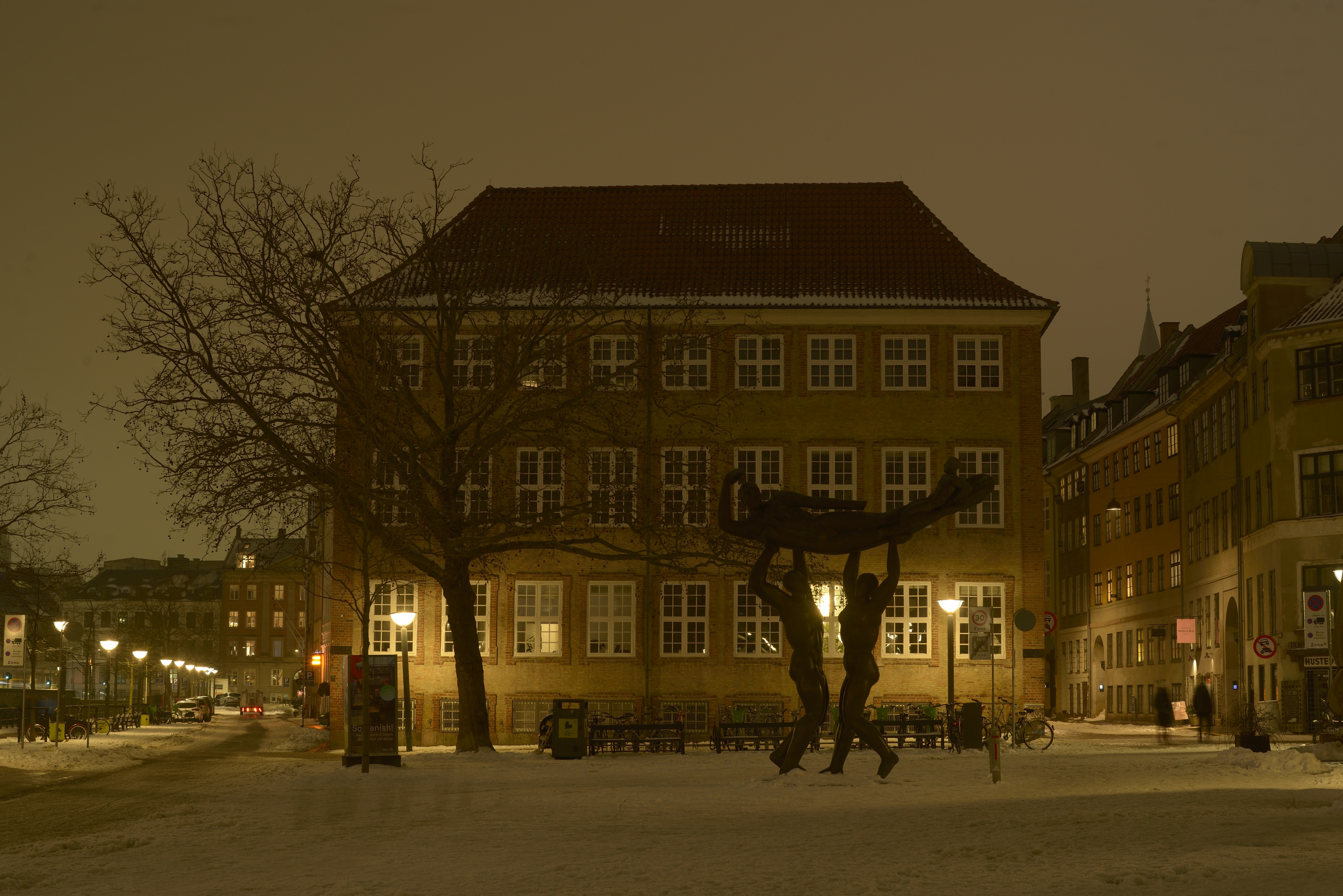 Snowy town square with building and sculpture at night
