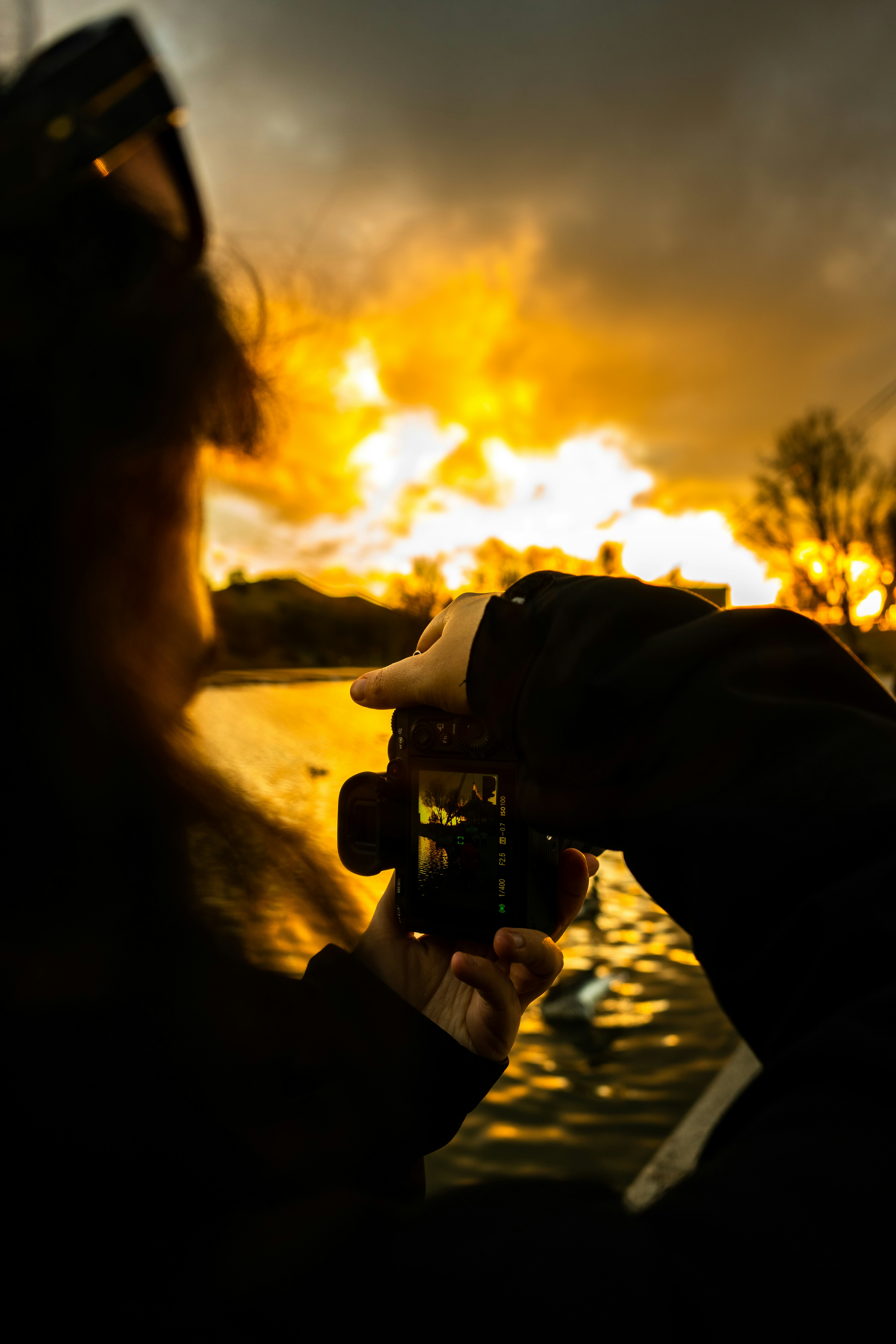 Person taking a picture of a vibrant sunset over water.