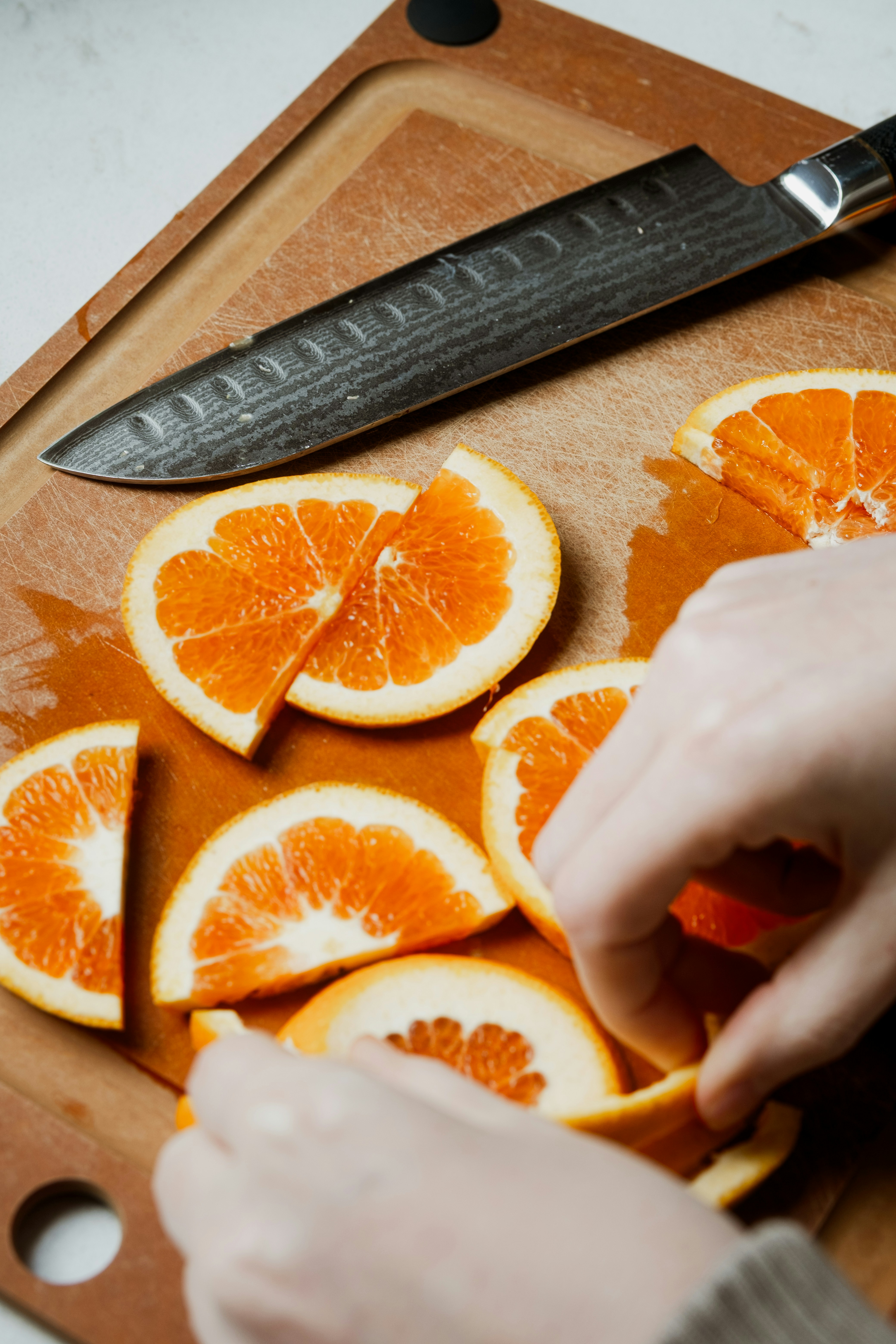 Hands arranging sliced oranges on a wooden cutting board.