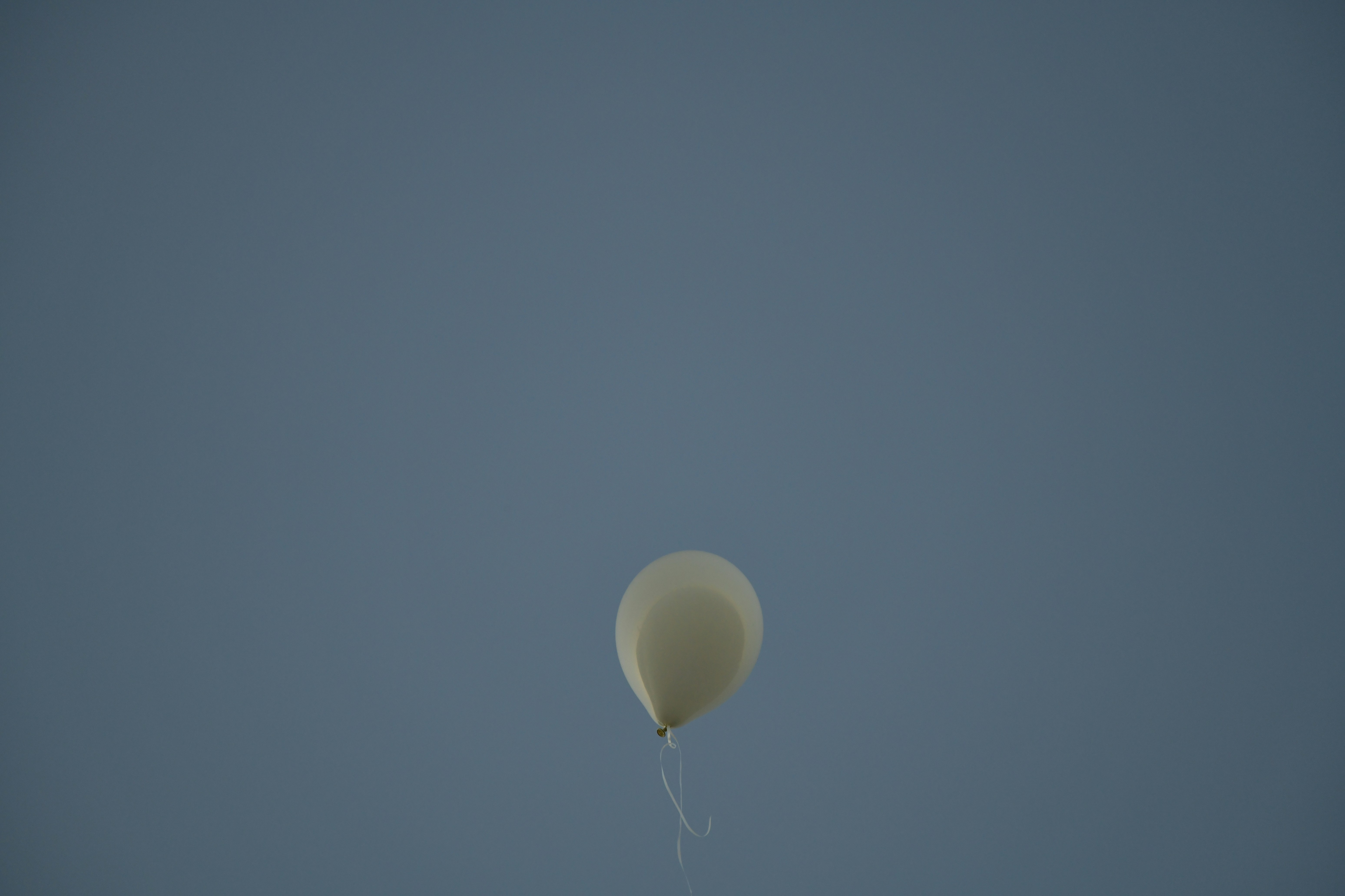 Ein einzelner weißer Ballon schwebt an einem klaren blauen Himmel.