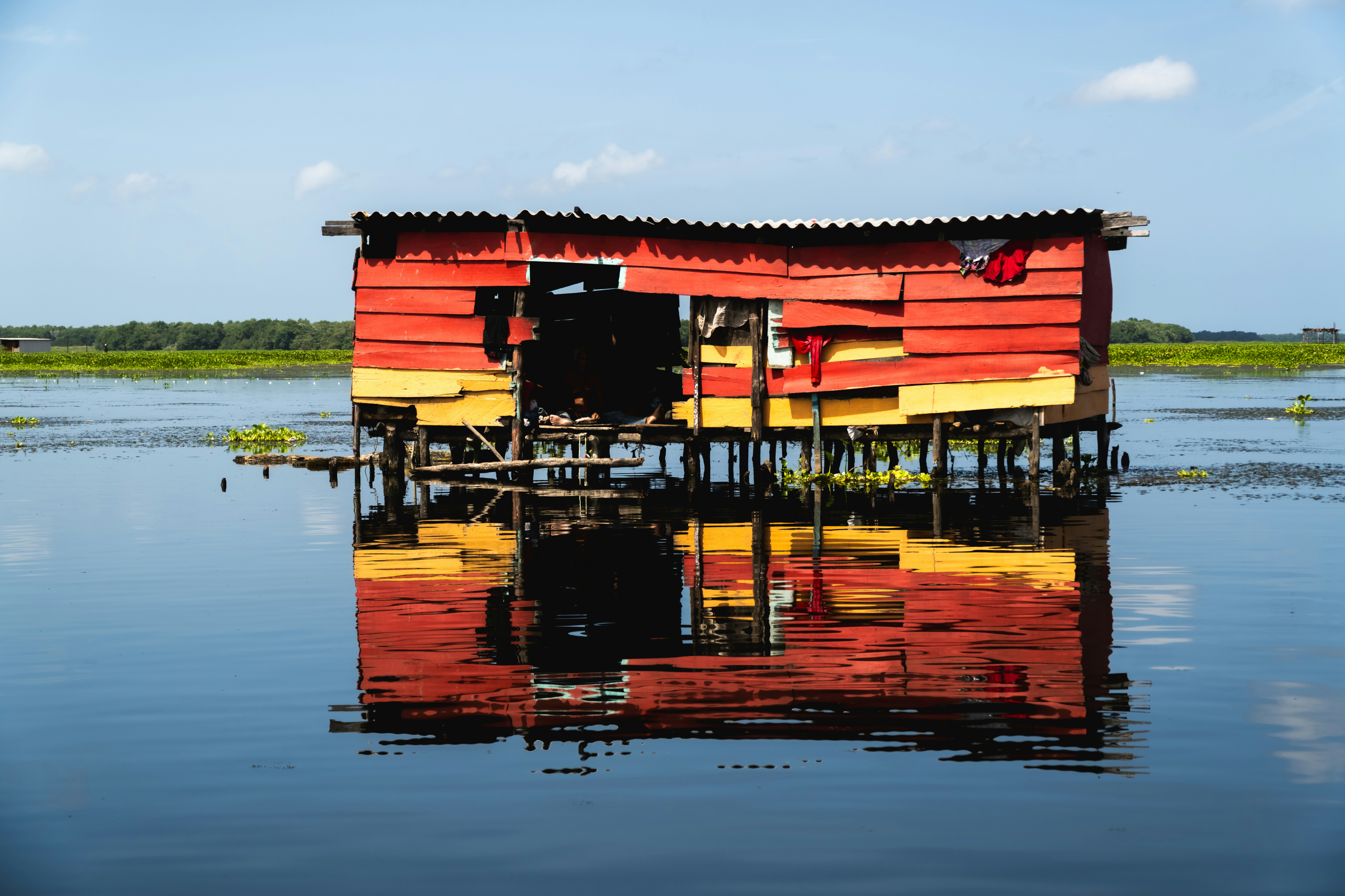 Una casa sobre pilotes roja y amarilla desgastada reflejada en el agua