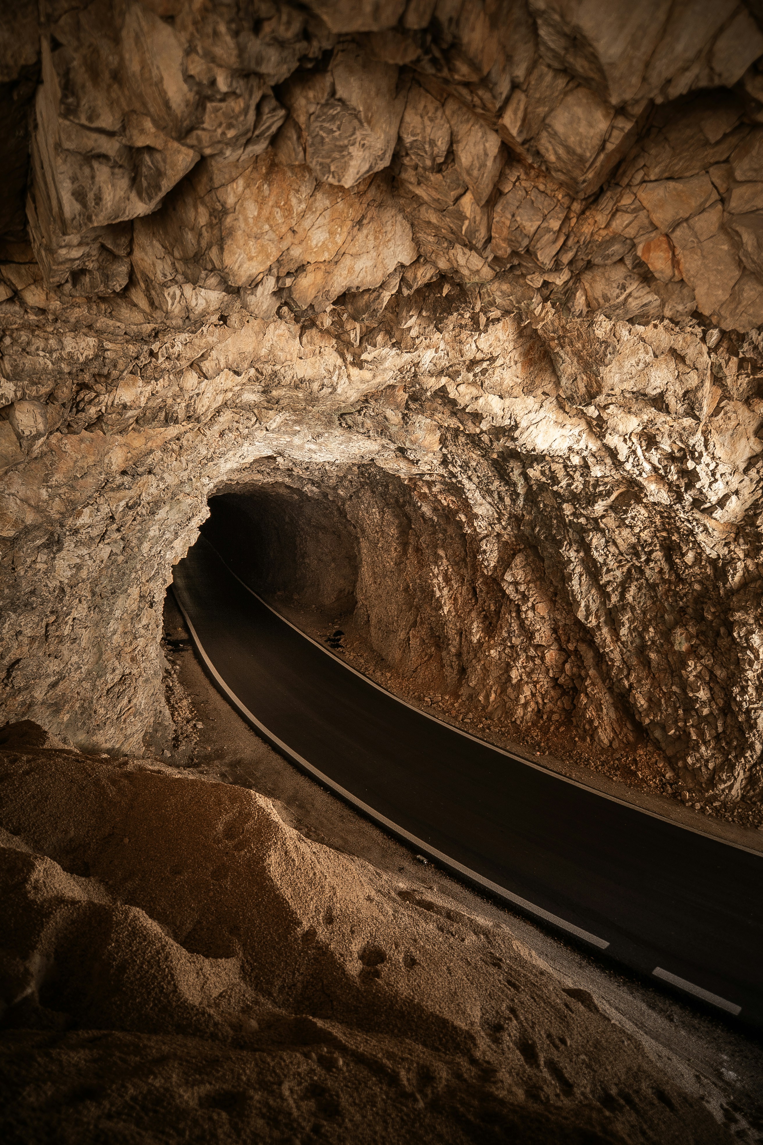 A dark road curves through a rocky cave tunnel.