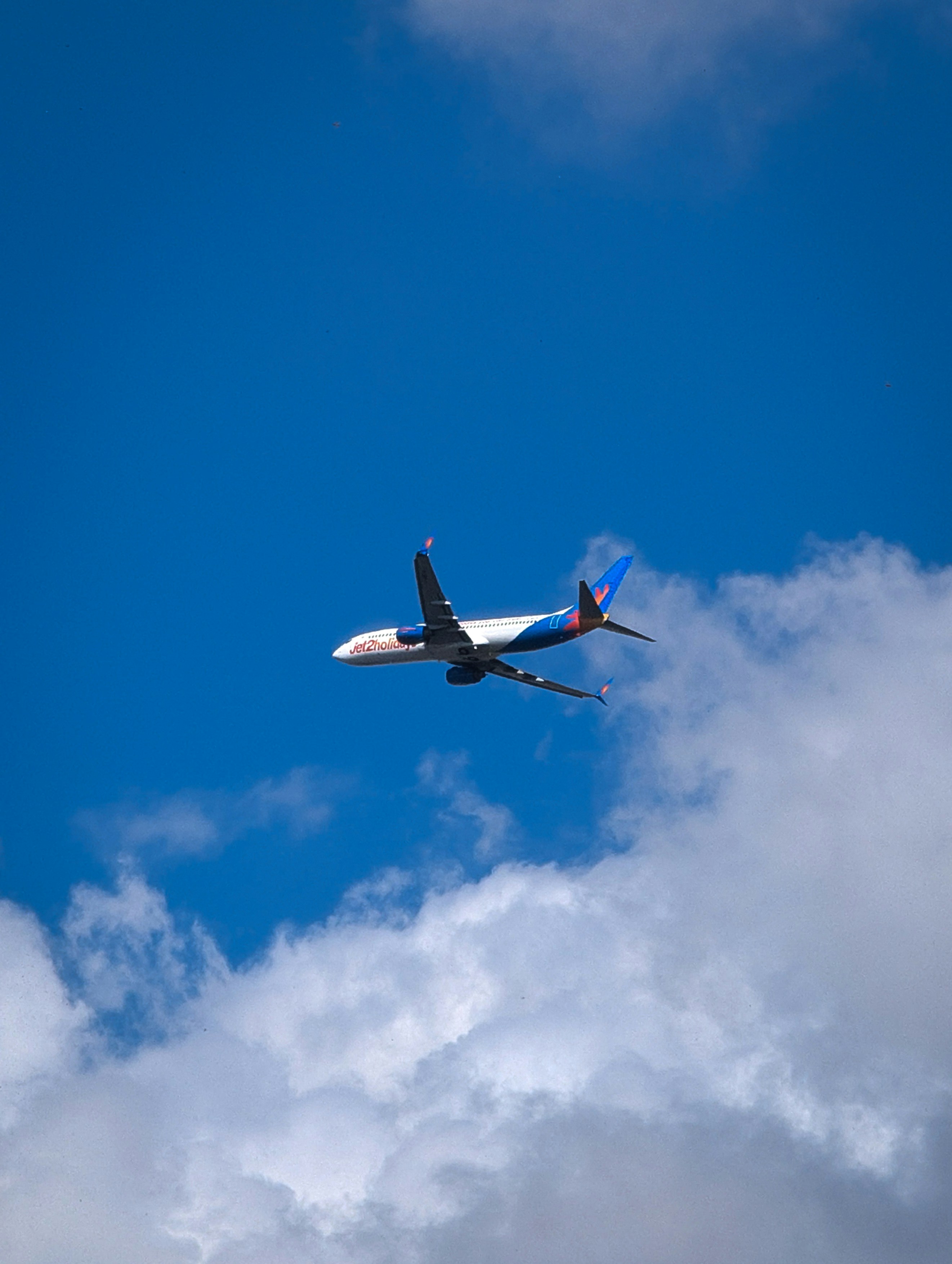 Airplane flying through a bright blue sky with clouds