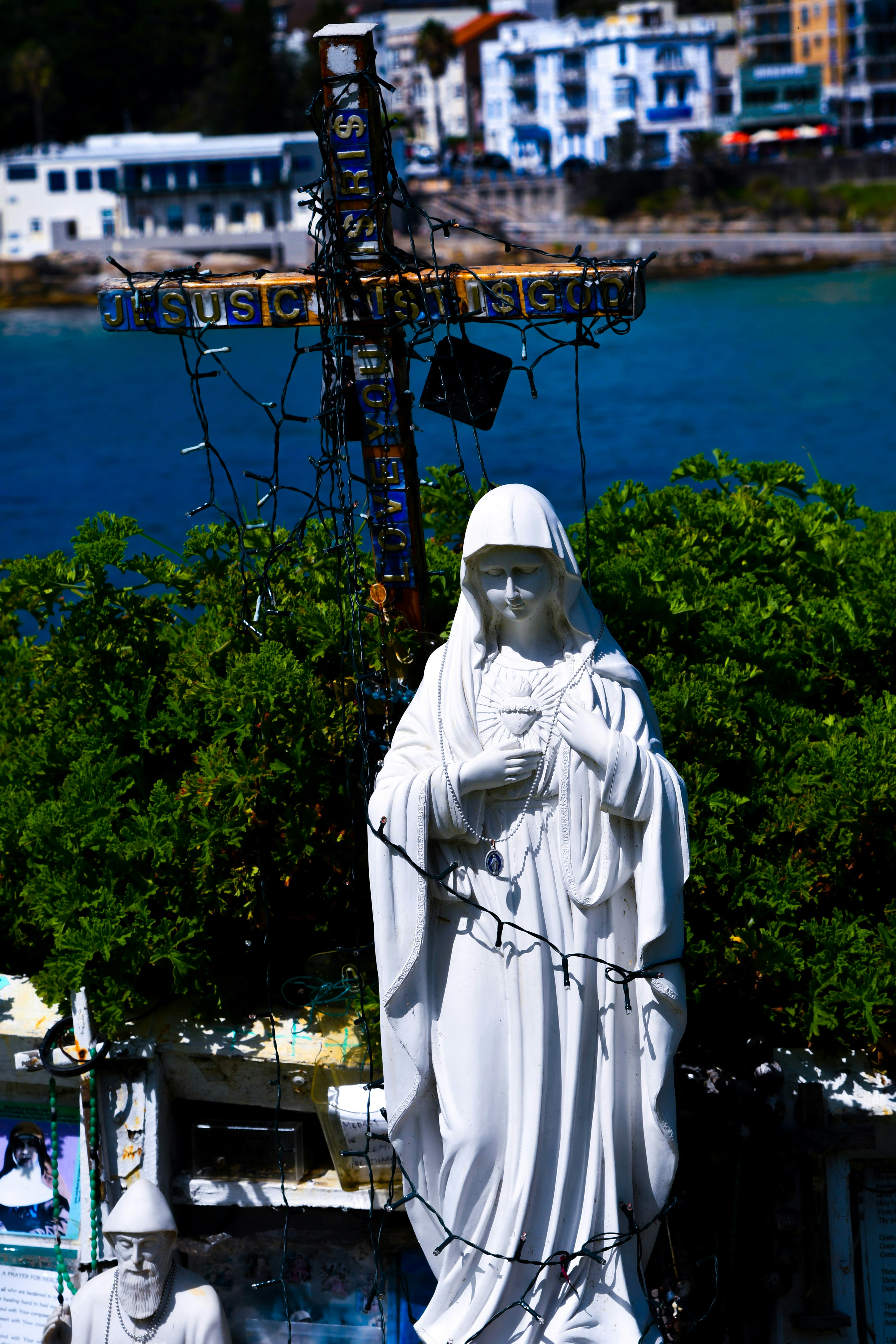Statue of mary with a cross and ocean background.