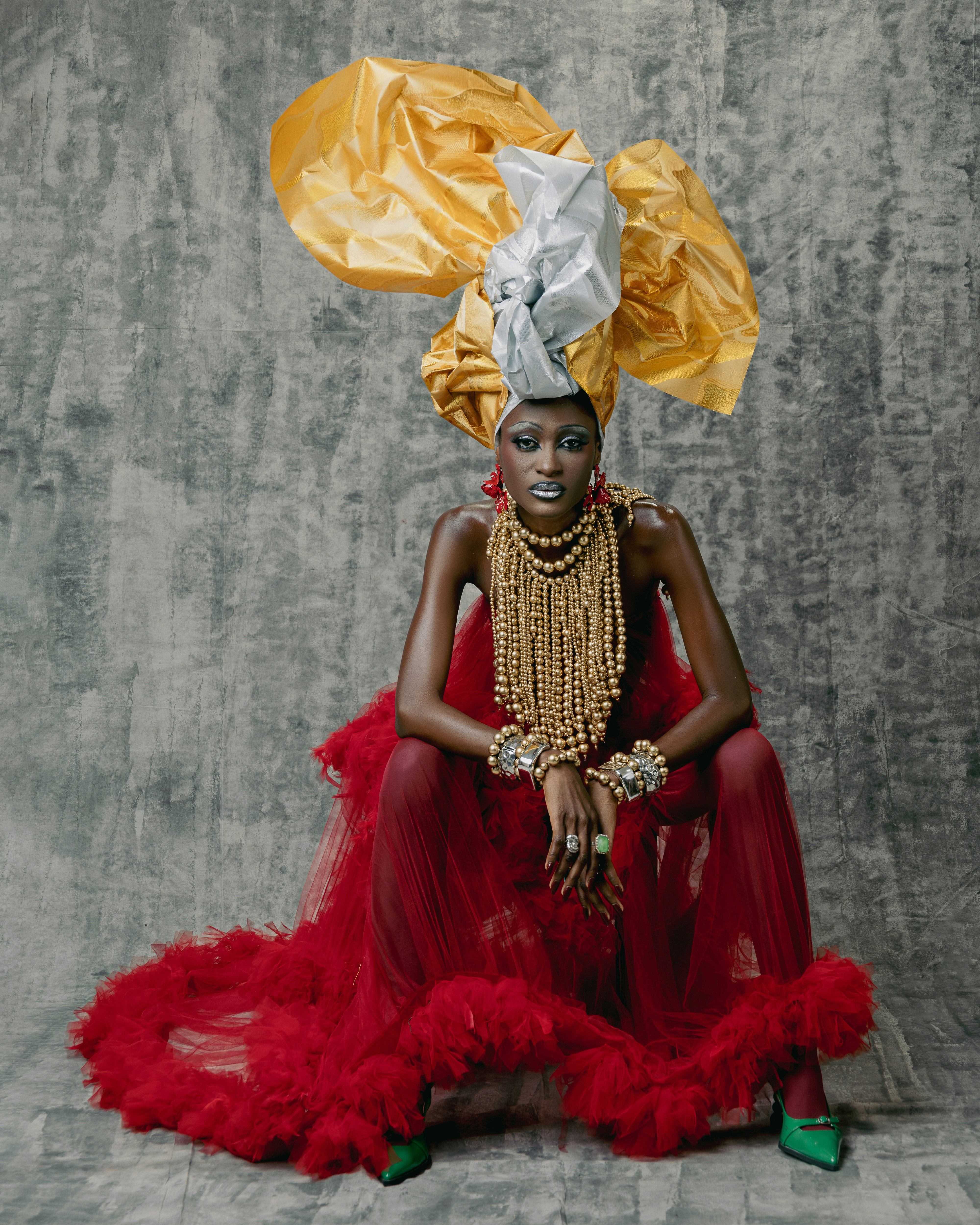 華やかな頭飾りと赤いドレスを身にまとった女性が優雅にポーズをとっています。