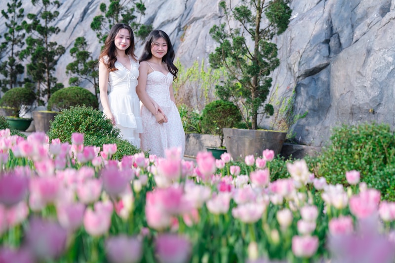 Two women in white dresses amidst pink tulips
