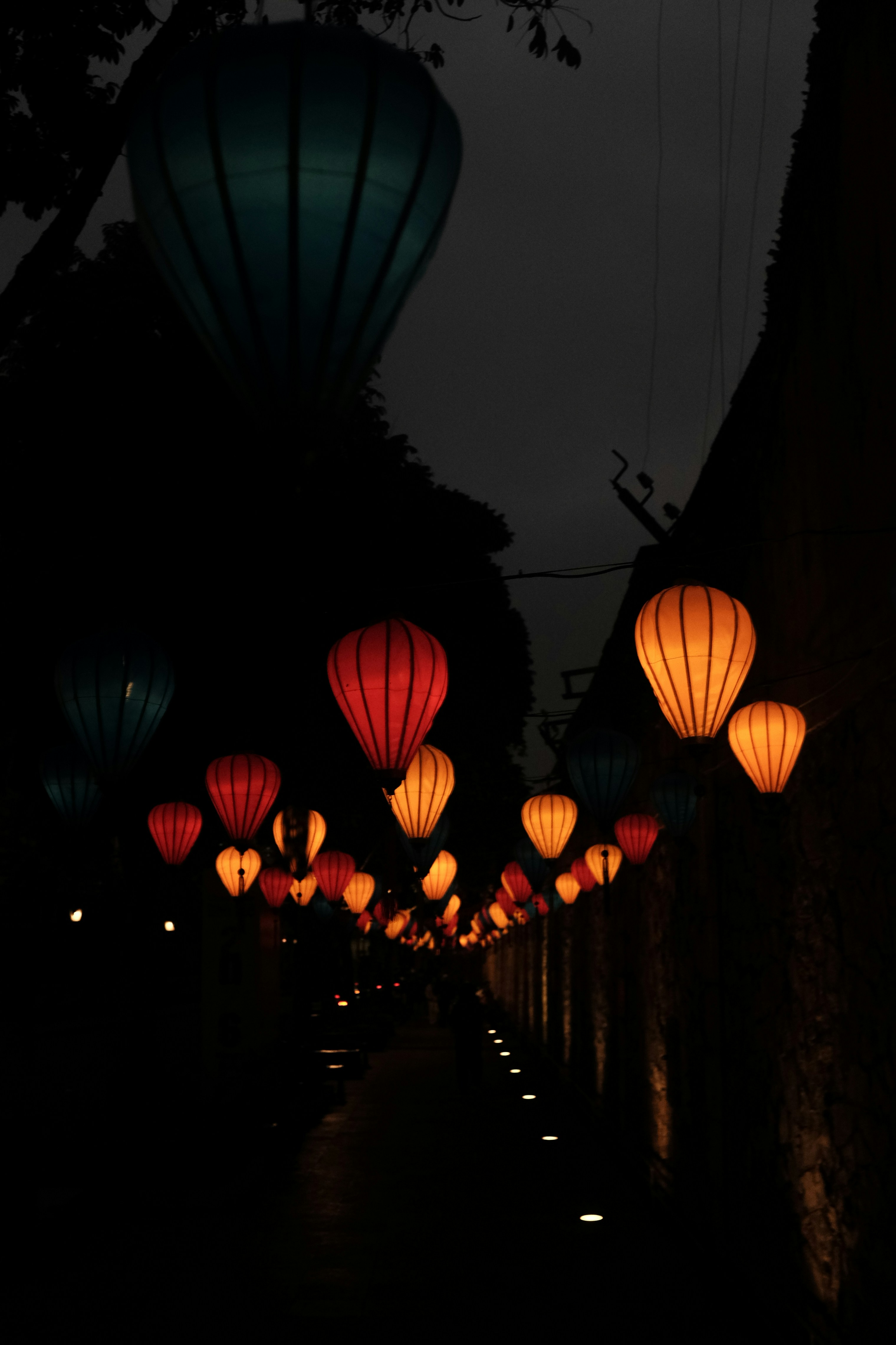 Colorful lanterns illuminate a dark pathway at night.