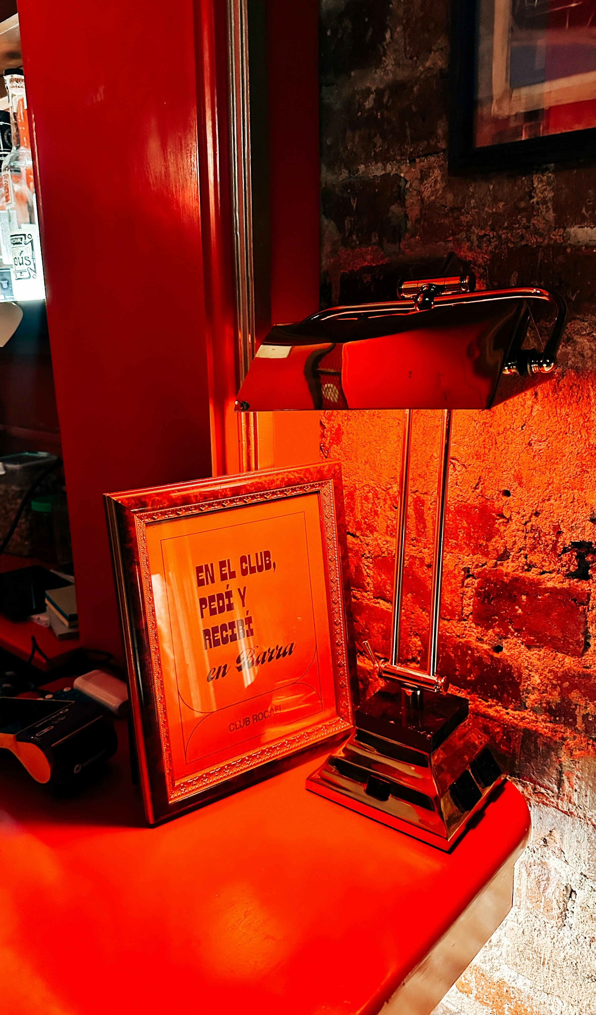 A framed sign and a red lamp on a table.