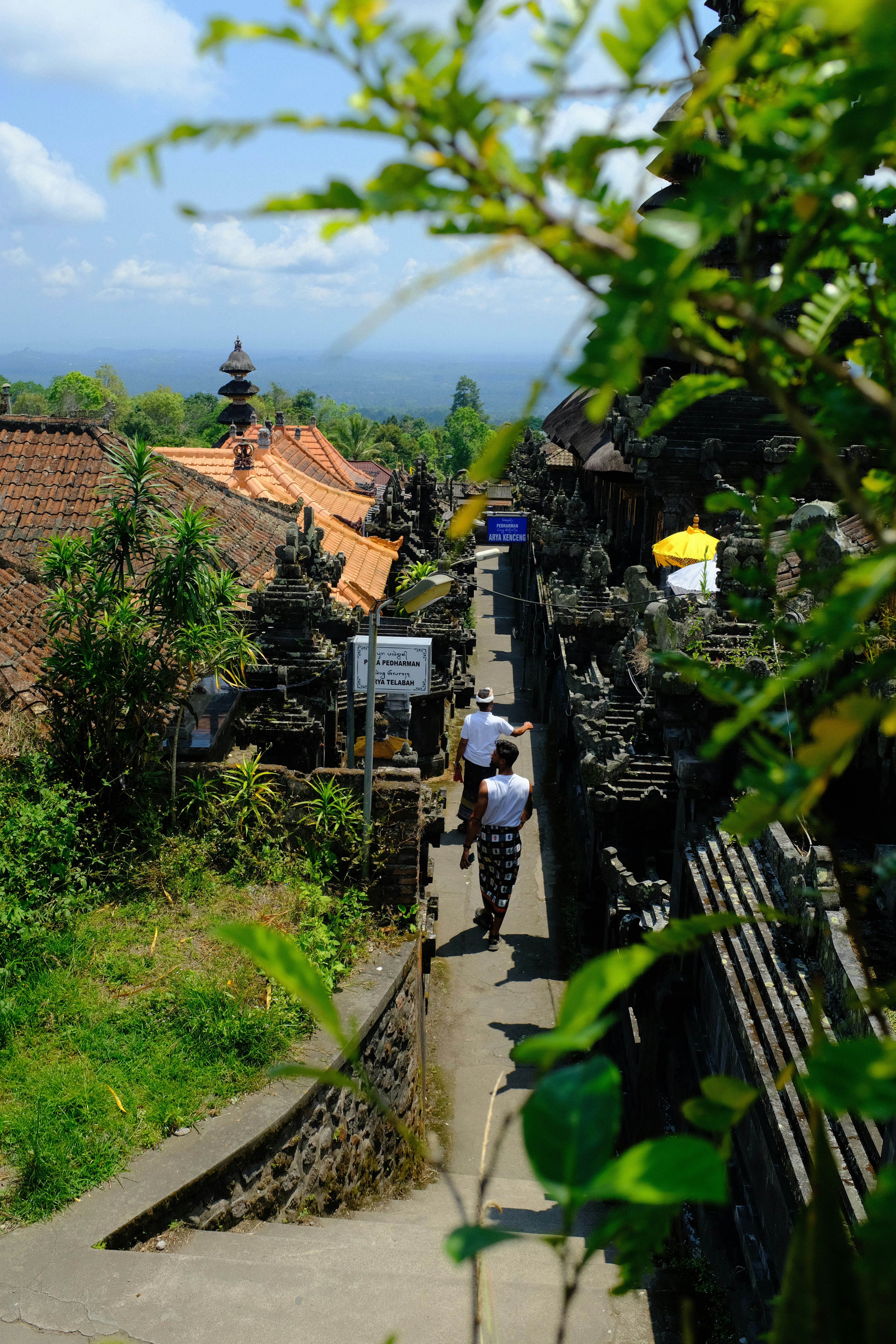 Two people walk along a path in a balinese village.