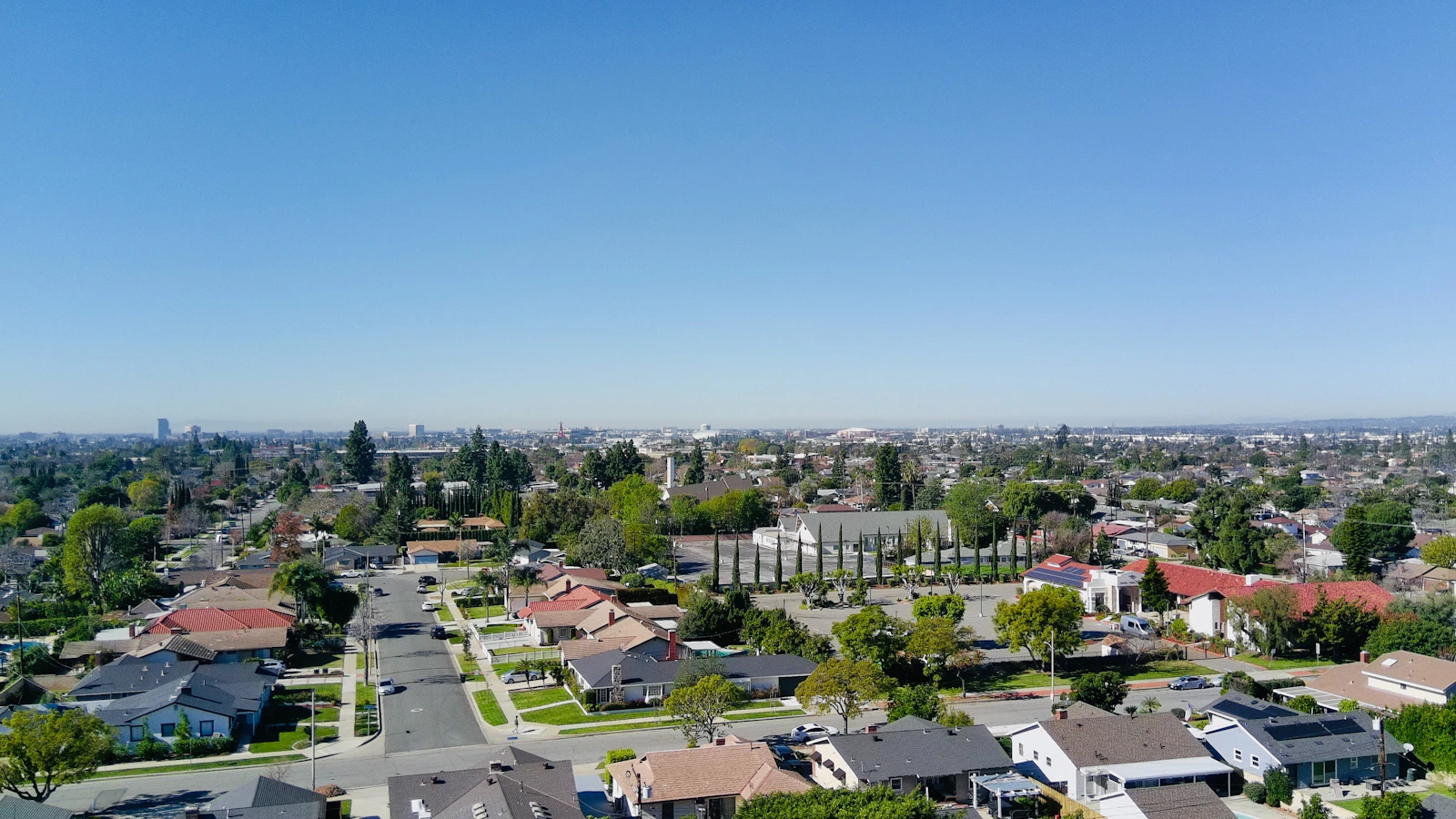 Suburban neighborhood street lined with houses and mature trees under a clear sky