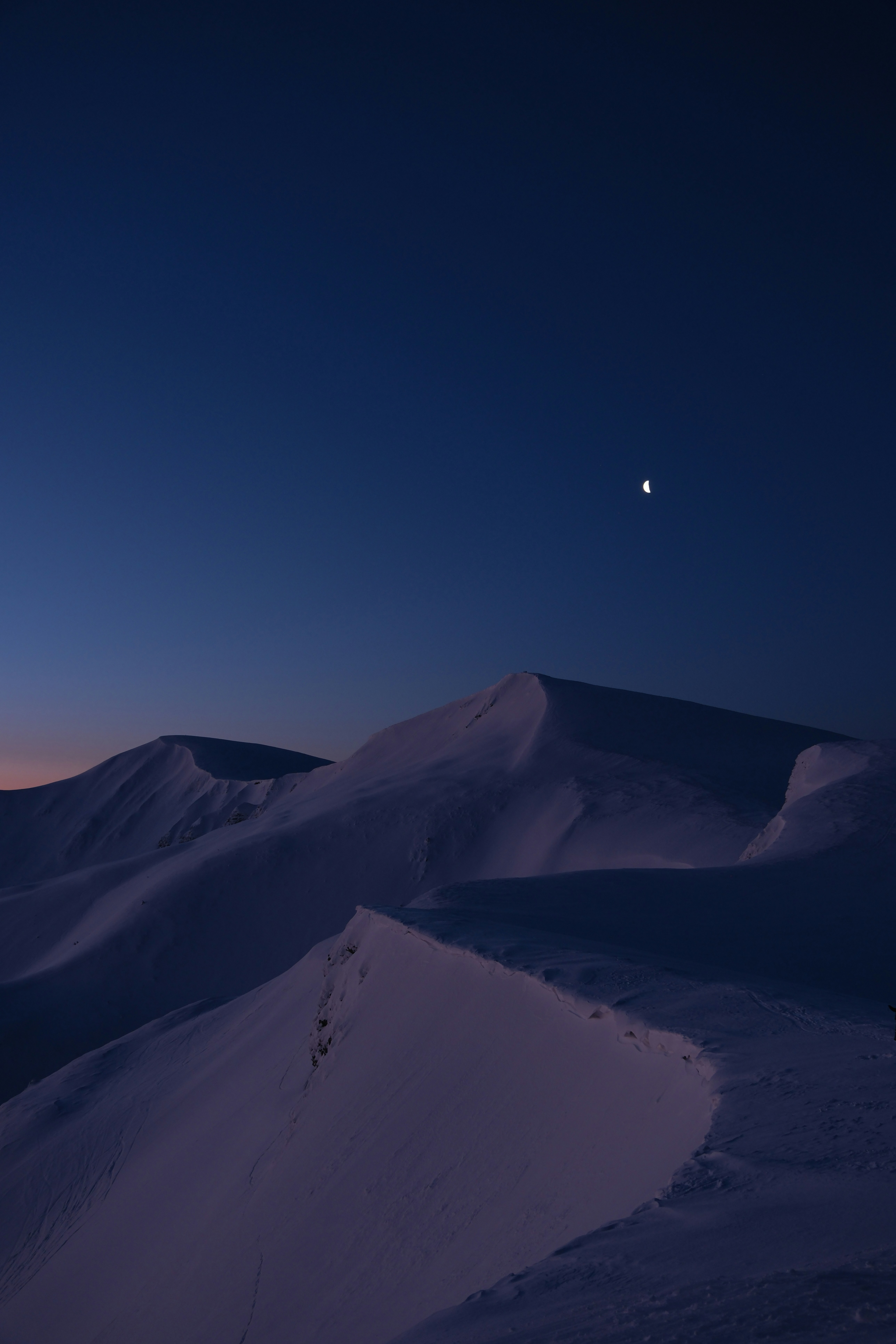 Snowy mountain range under a dark blue twilight sky.