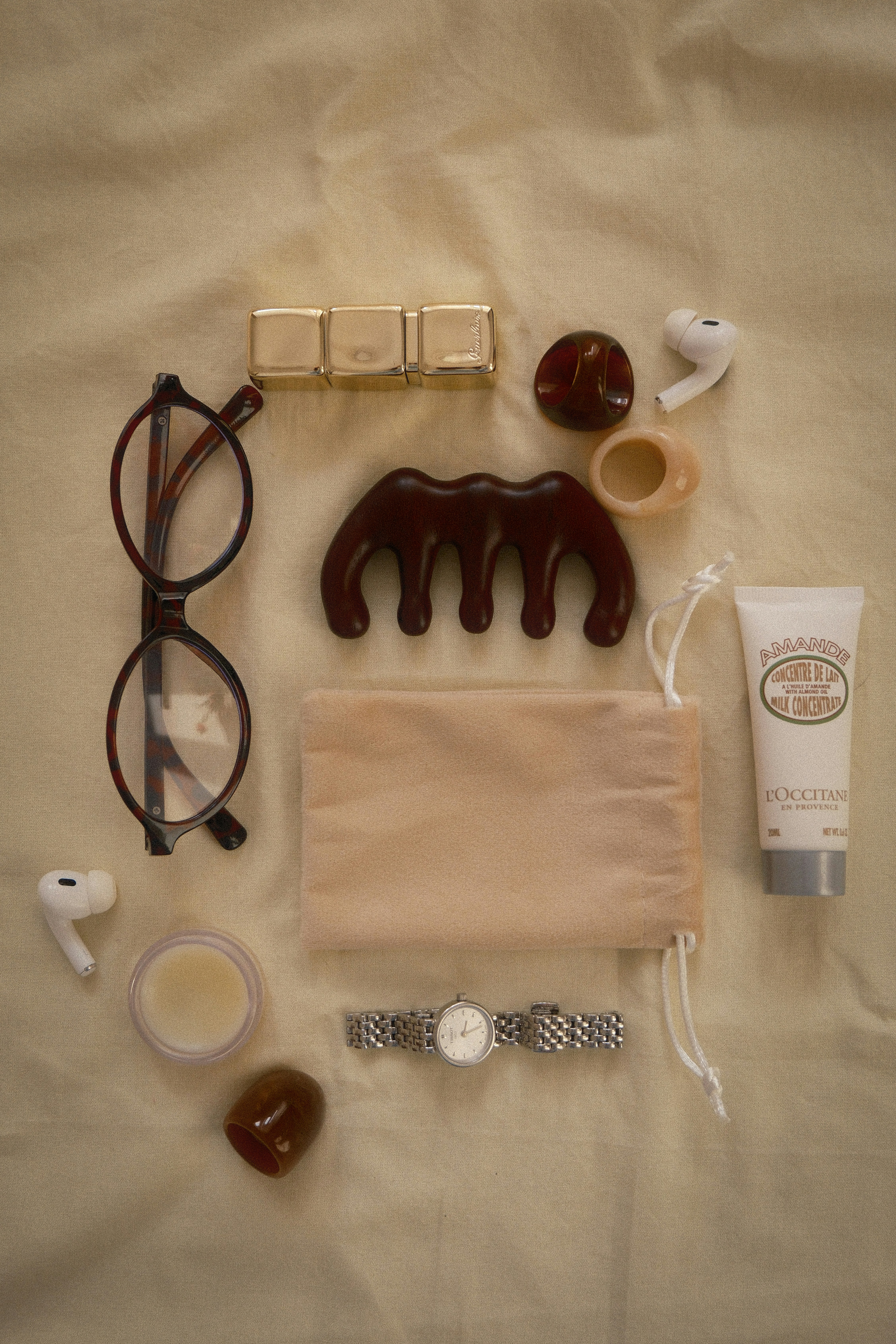 Eyeglasses, comb, lotion, watch, and earbuds arranged flat lay.