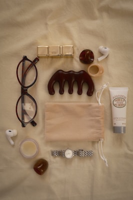 Eyeglasses, comb, lotion, watch, and earbuds arranged flat lay.