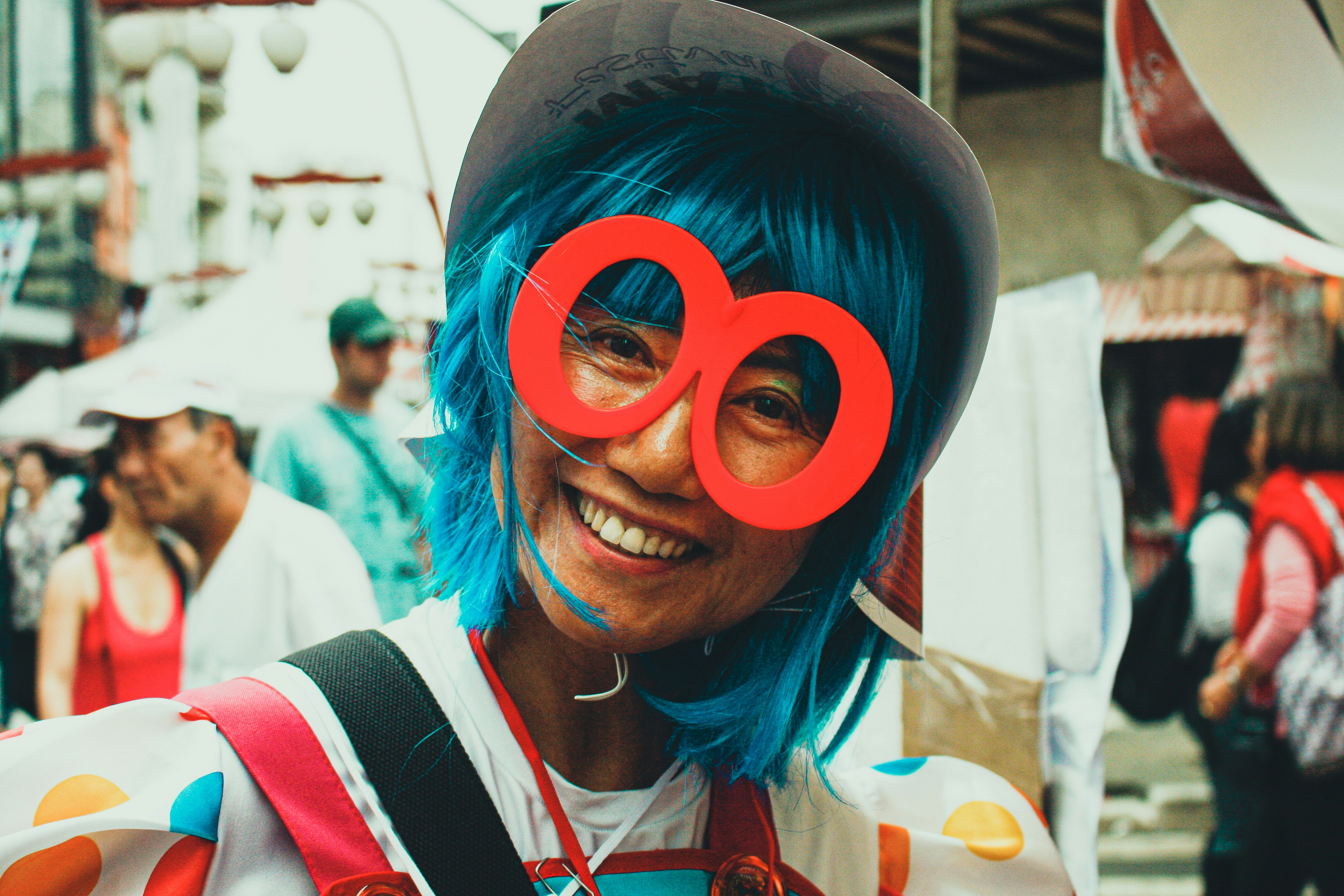 Seseorang dengan rambut biru dan kacamata merah tersenyum