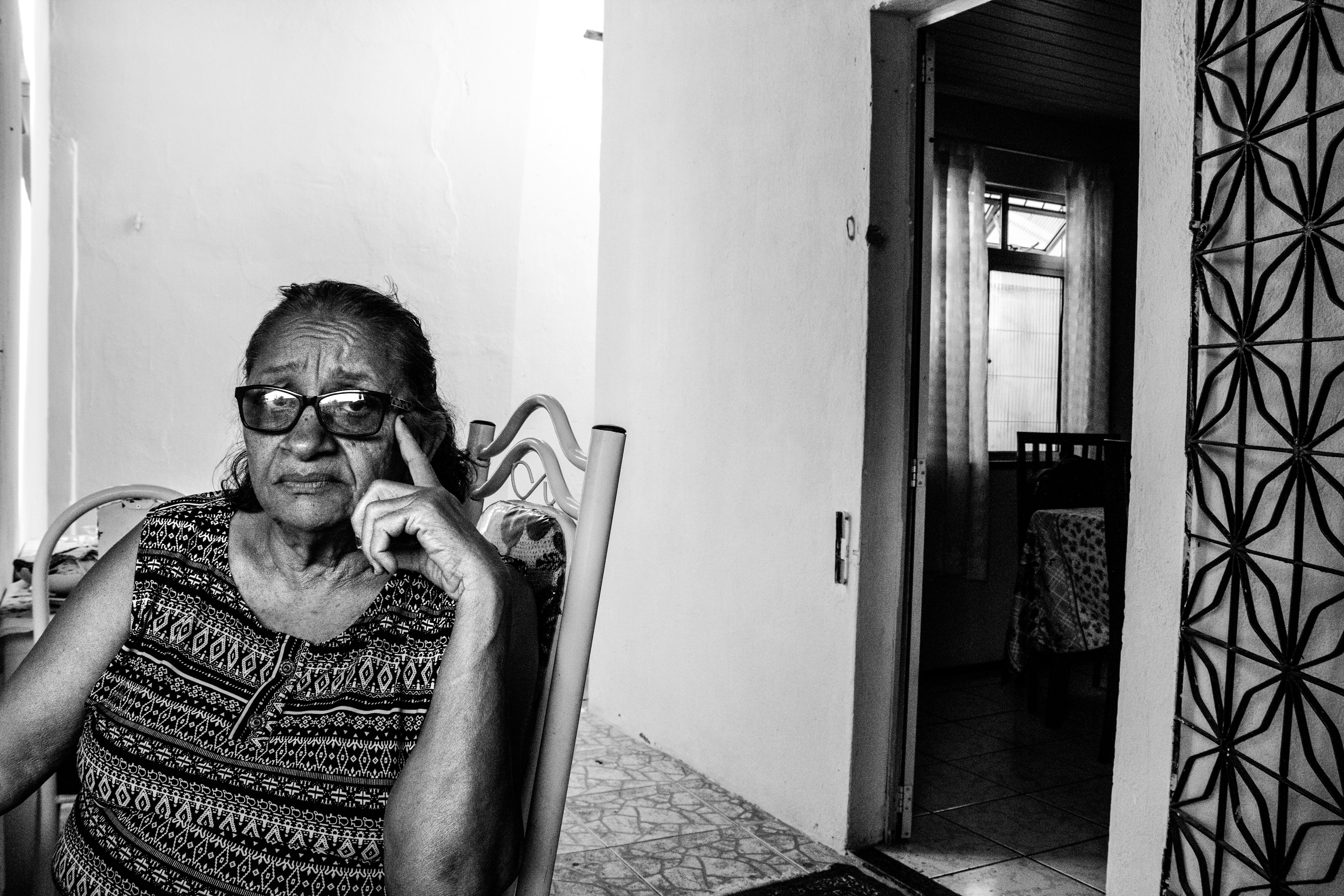 Elderly woman with glasses sitting in a chair.