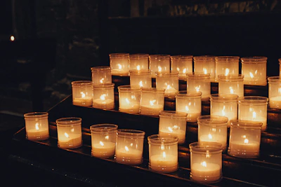Rows of lit votive candles in glass holders