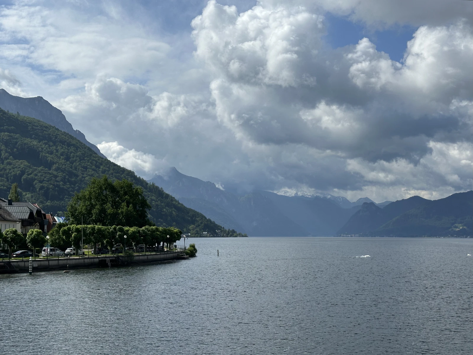 Photograph of Traunsee below steep green mountains and towering white clouds near Gmunden.
