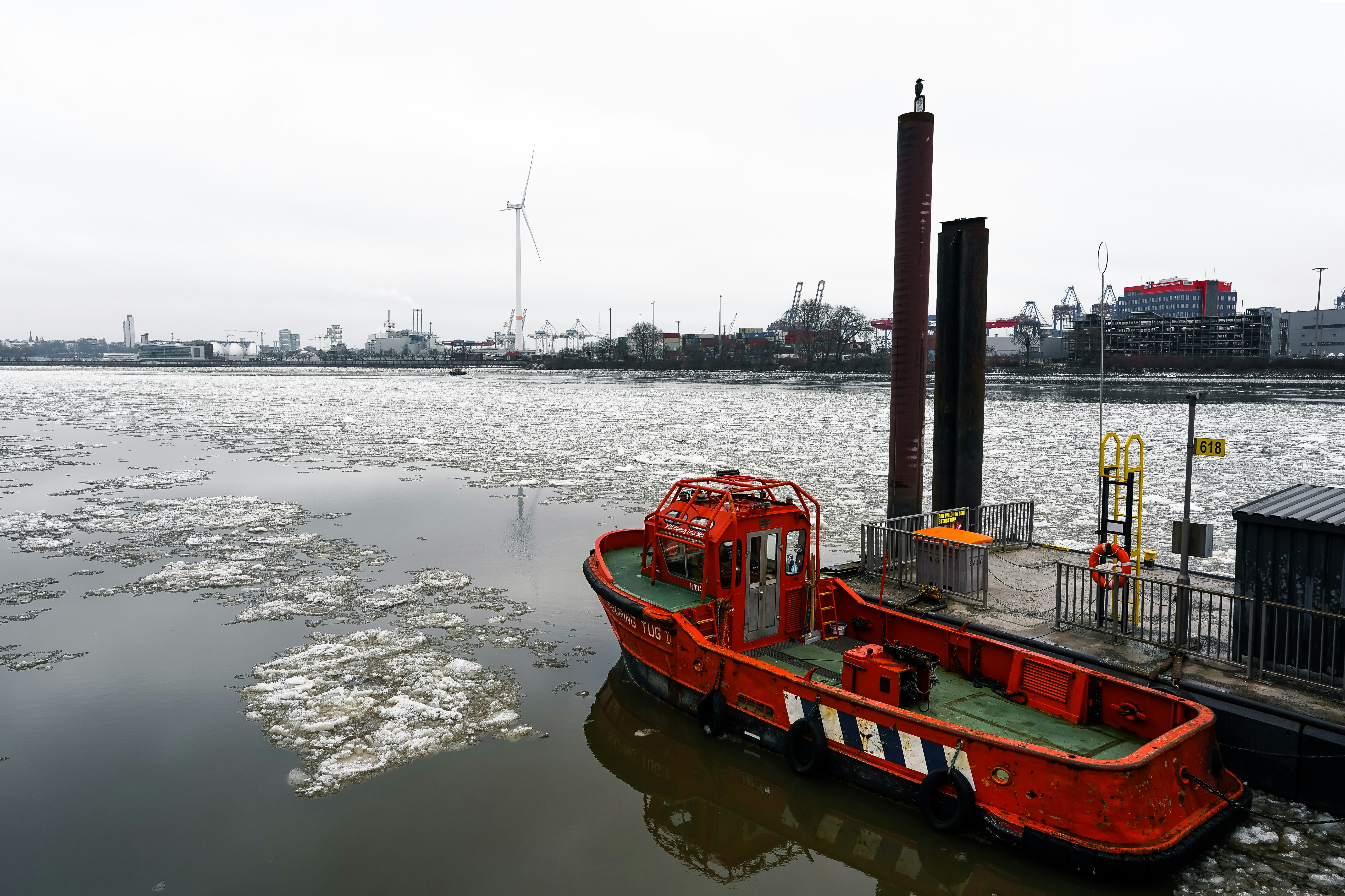 Red boat docked in icy water with industrial background