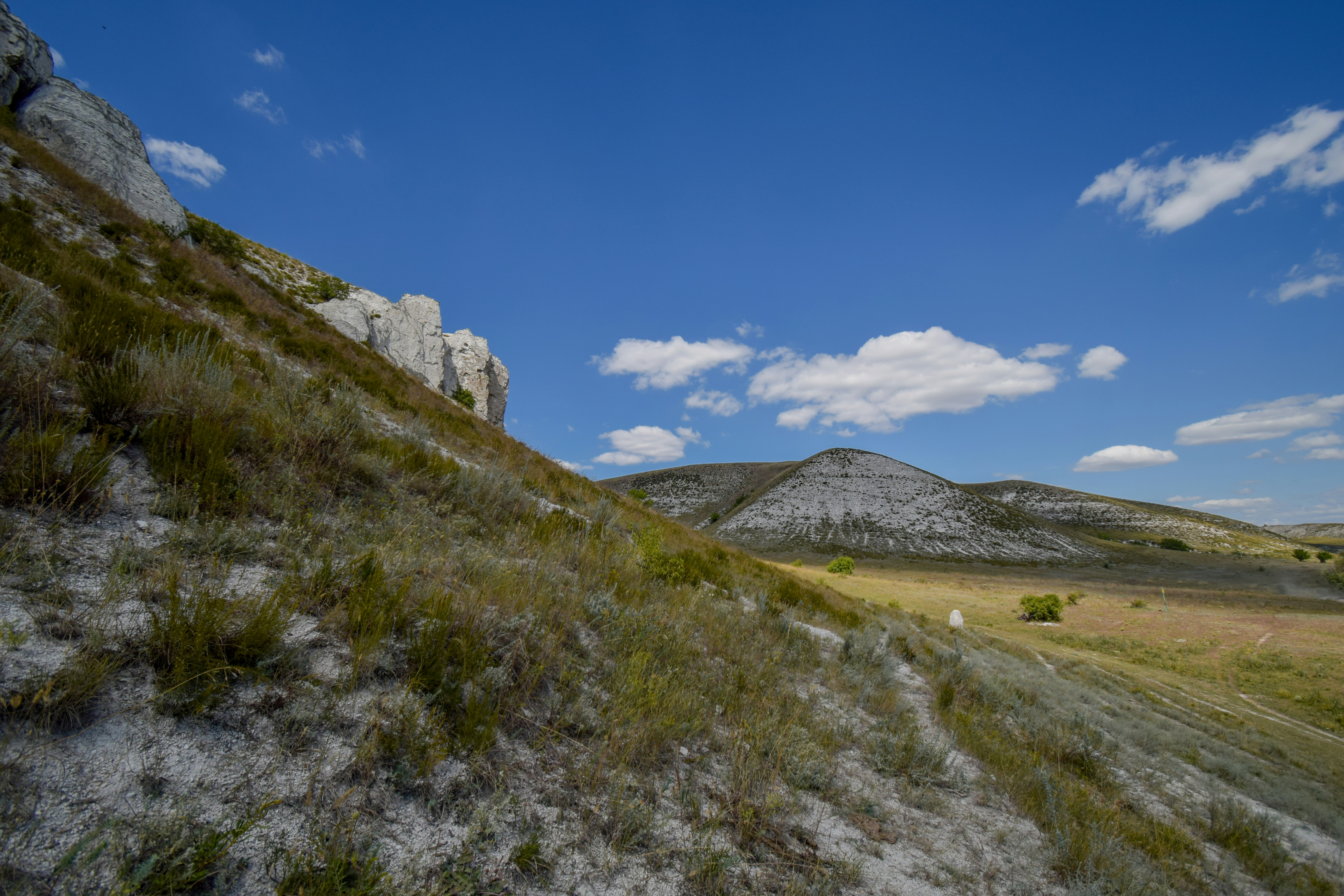 Grassy hillside with distant mountains under blue sky.