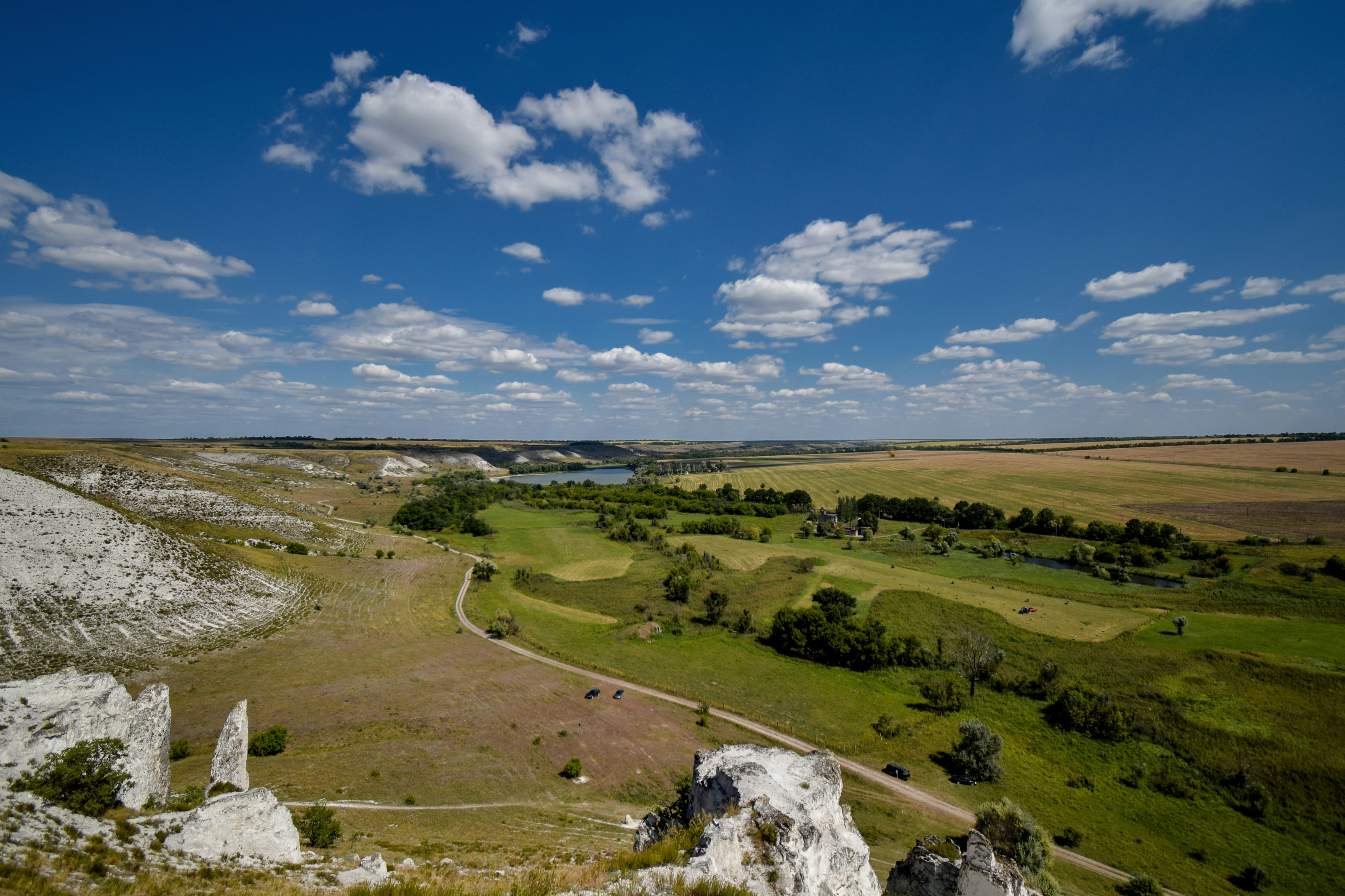 Formações rochosas brancas vigiam um vale verde sob céu azul.