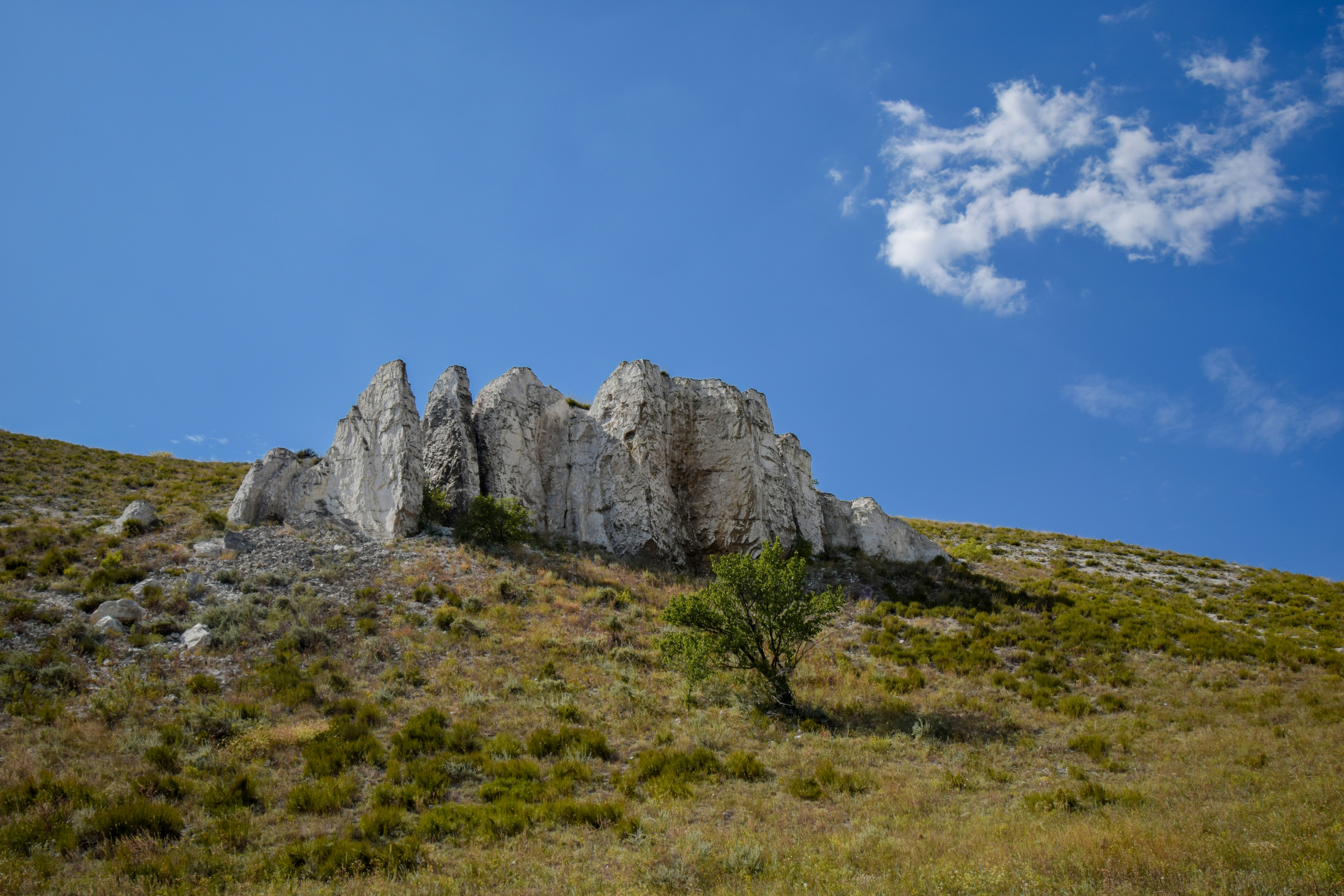 Jagged white rocks on a grassy hillside under blue sky