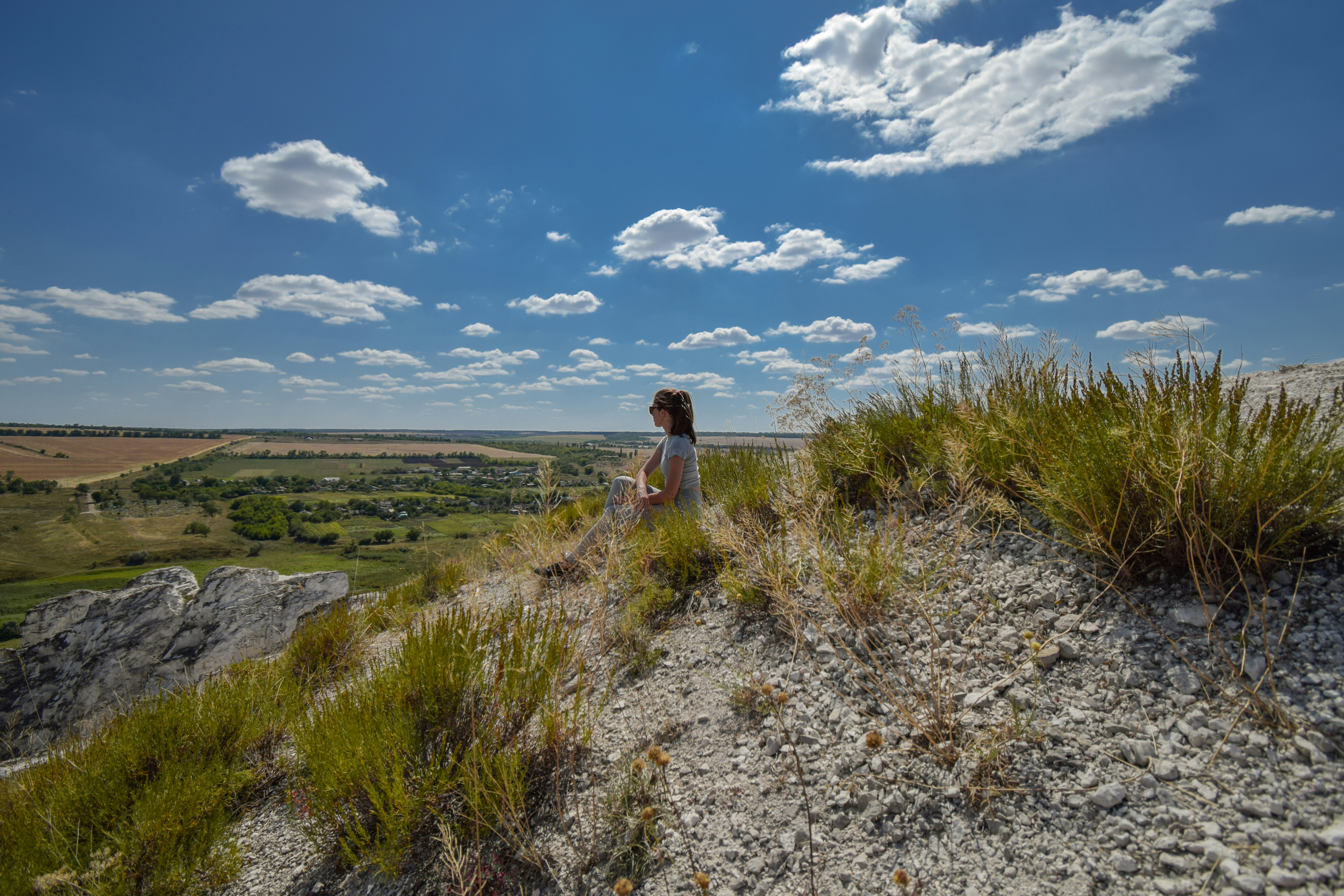 Uma pessoa senta-se em uma colina gramada com vista para um vale.