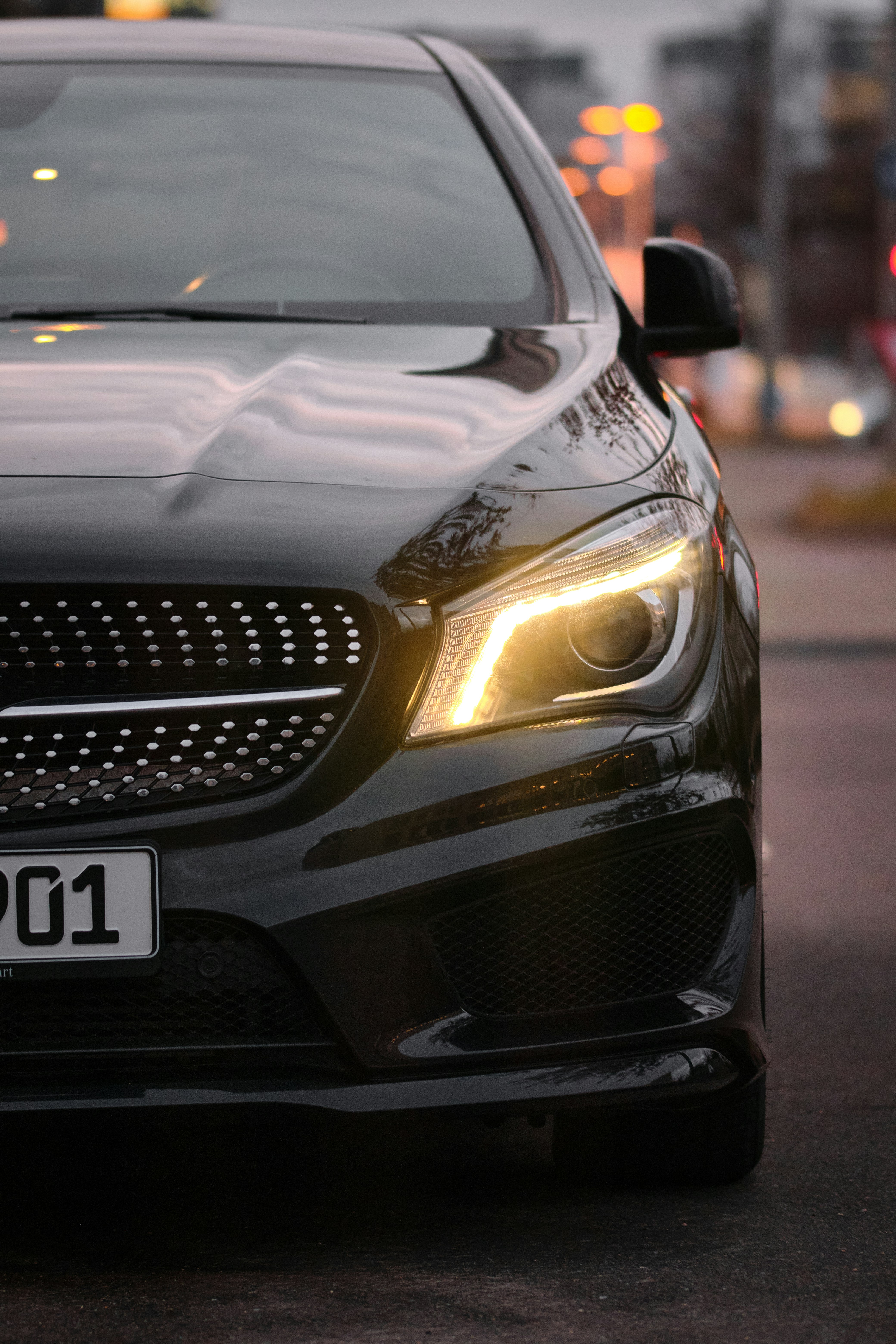 Black luxury car with illuminated headlights at dusk