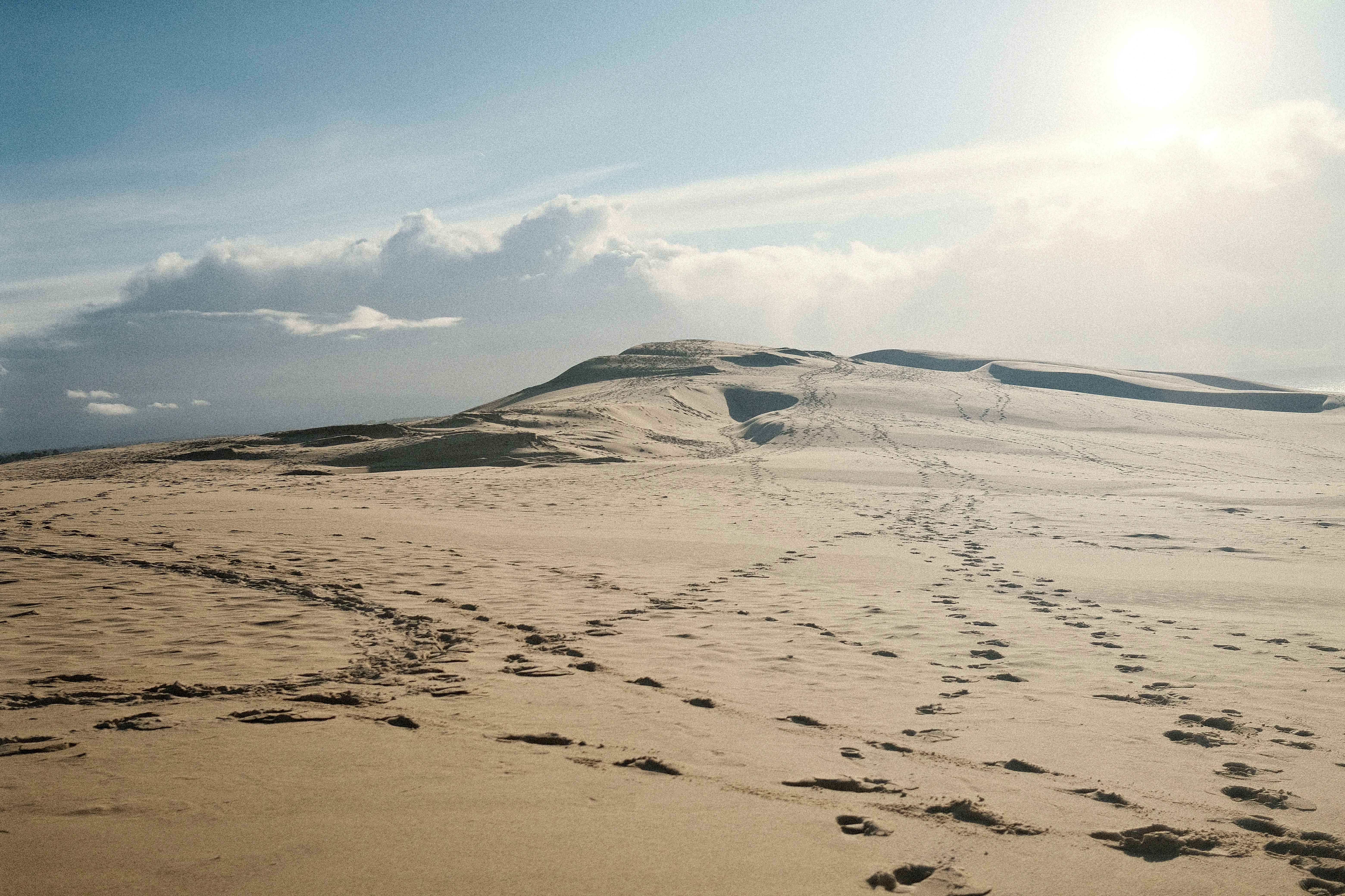 Footprints lead across a sandy dune under a bright sky