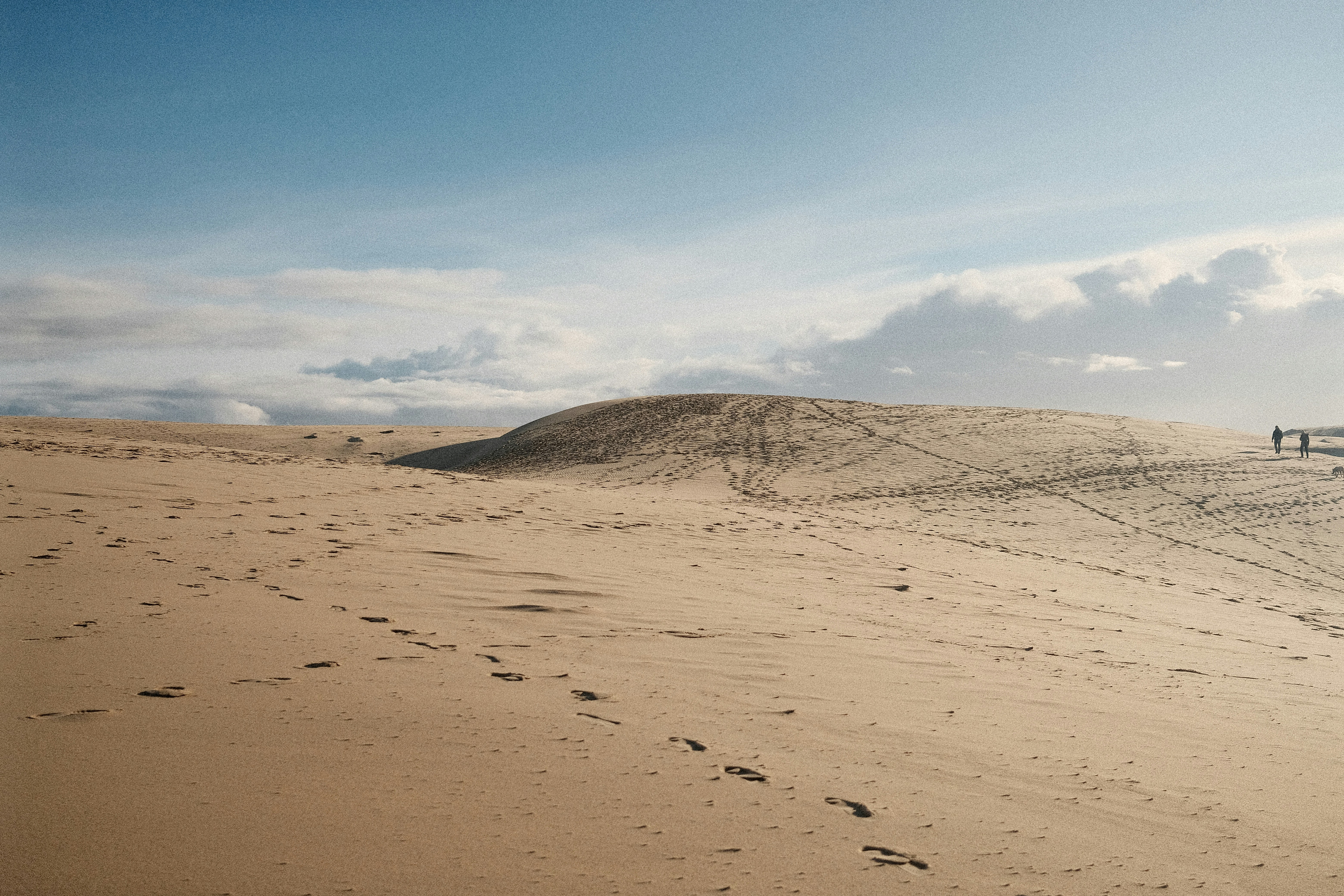Footprints on a sandy desert dune under a cloudy sky