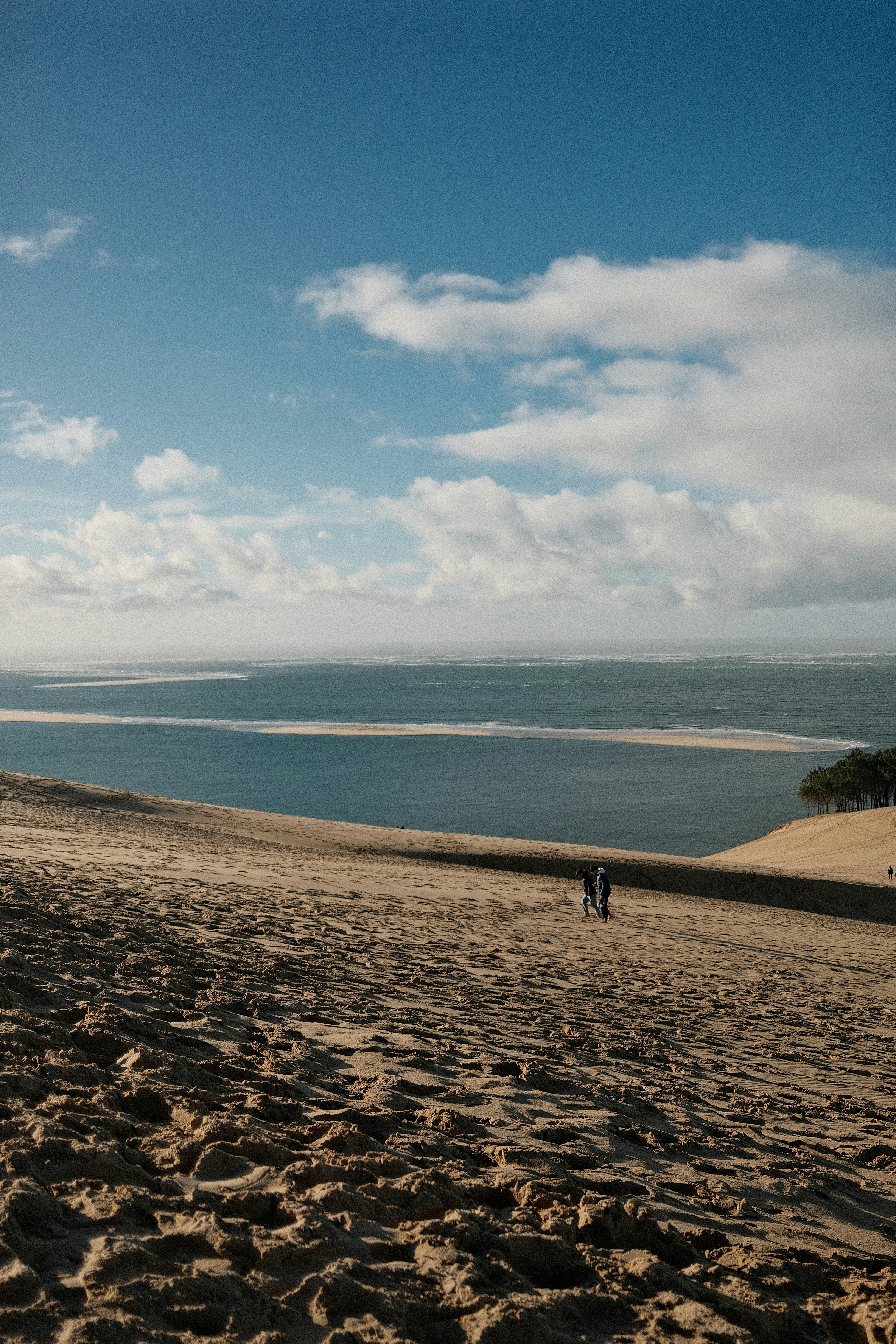 Zwei Personen gehen eine sandige Düne hinauf in Richtung Ozean.
