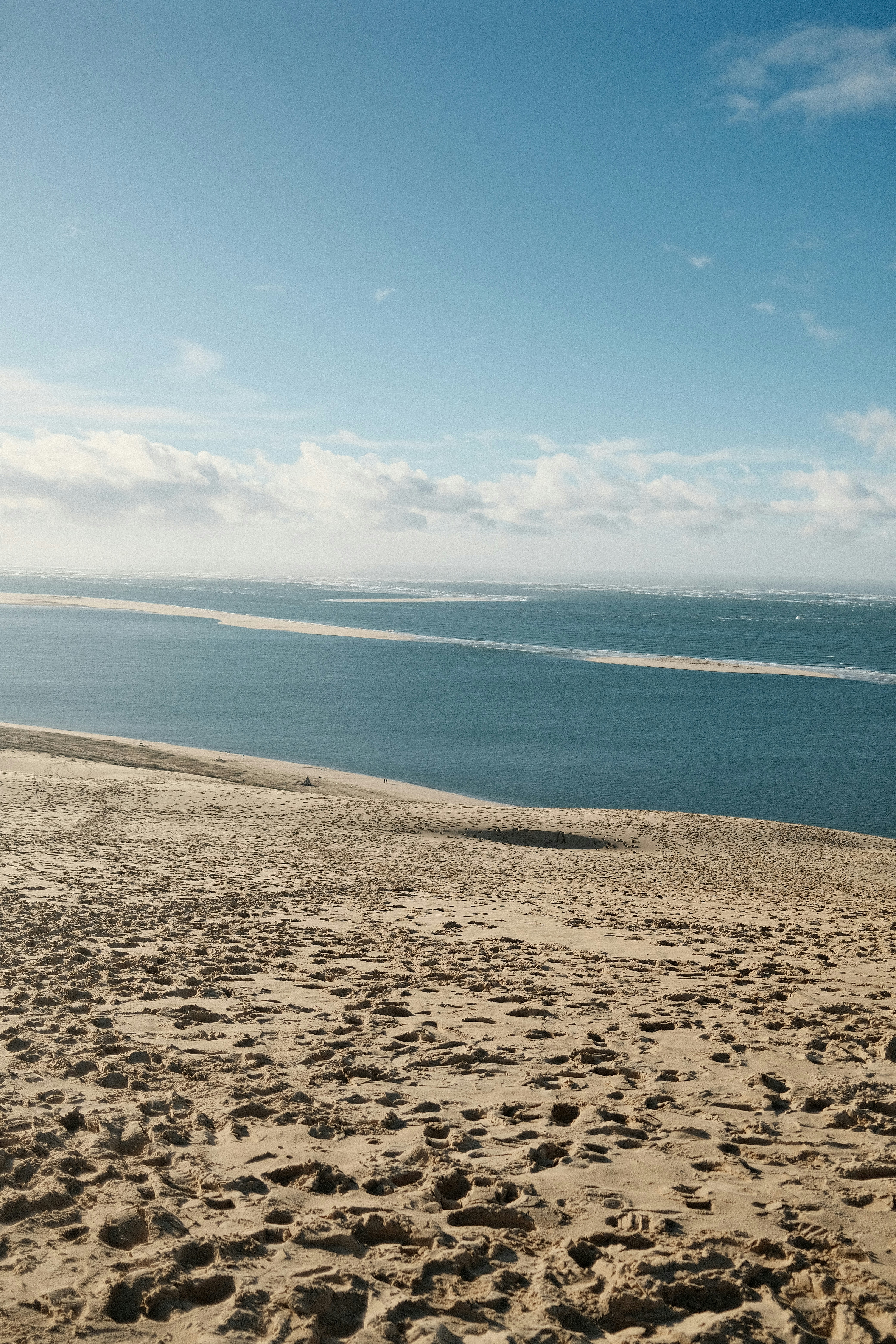 Sandy dunes meet calm blue ocean under a cloudy sky.