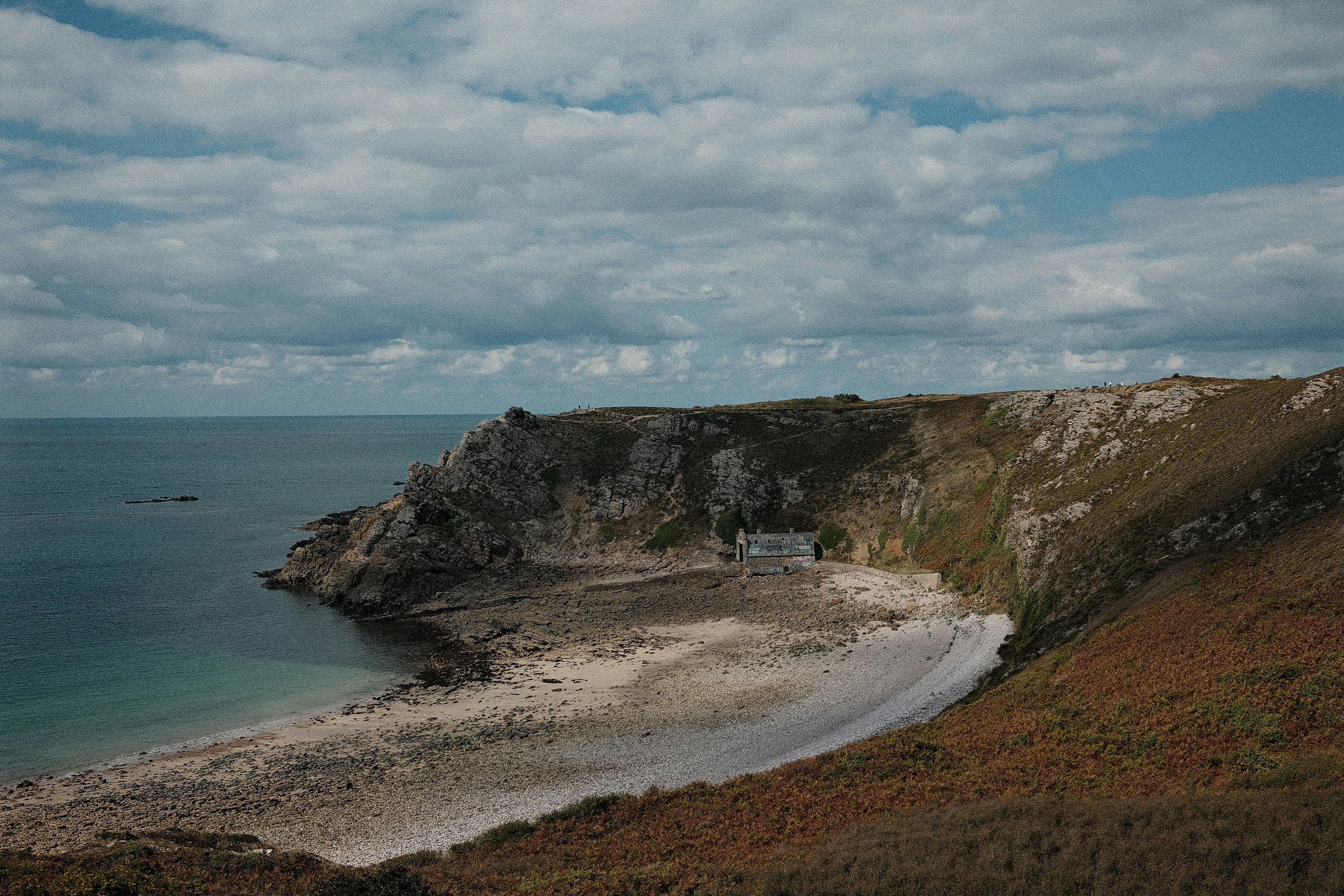 Secluded beach nestled beside rugged cliffs under cloudy sky