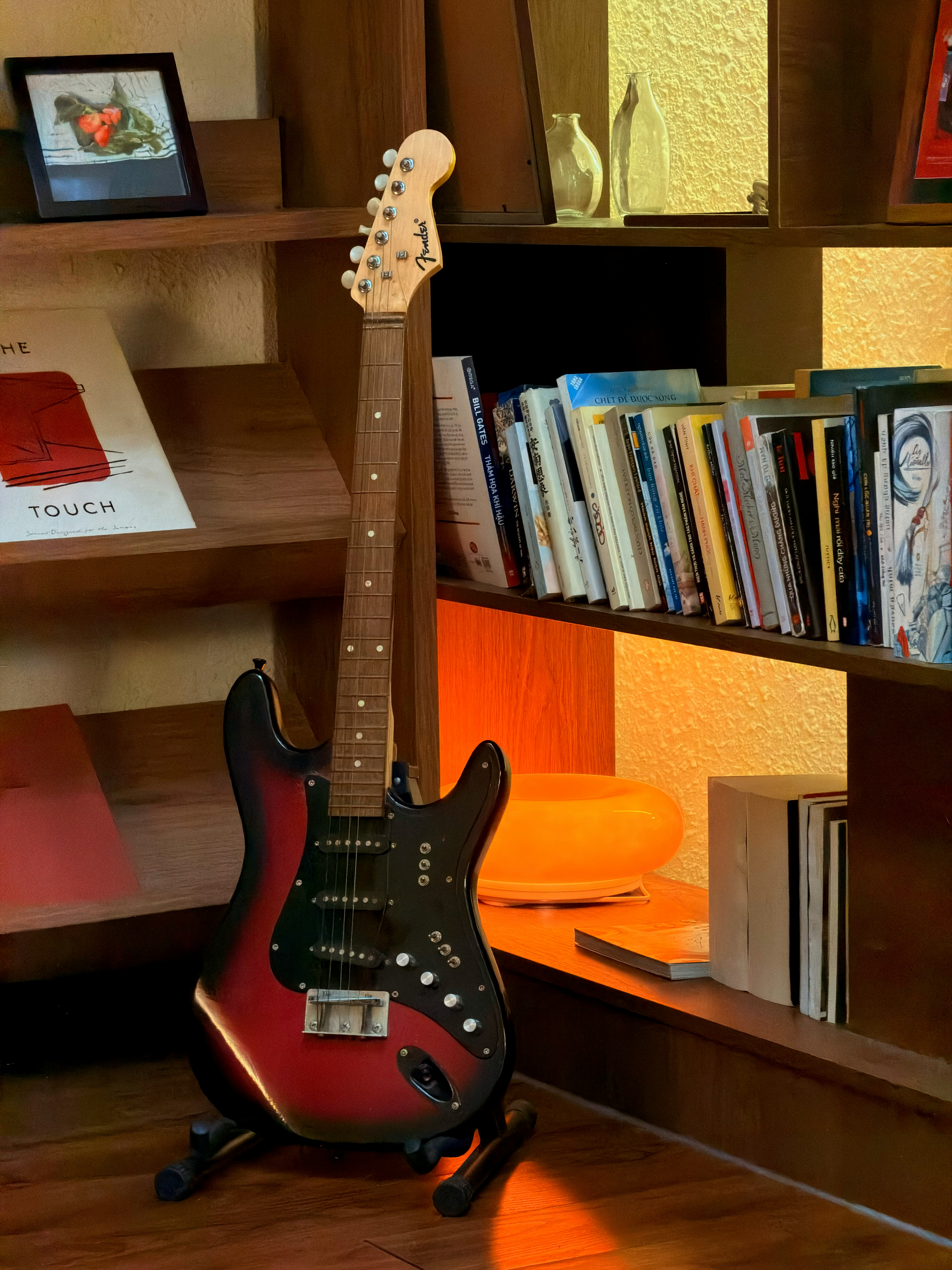 Electric guitar standing on a stand next to bookshelves