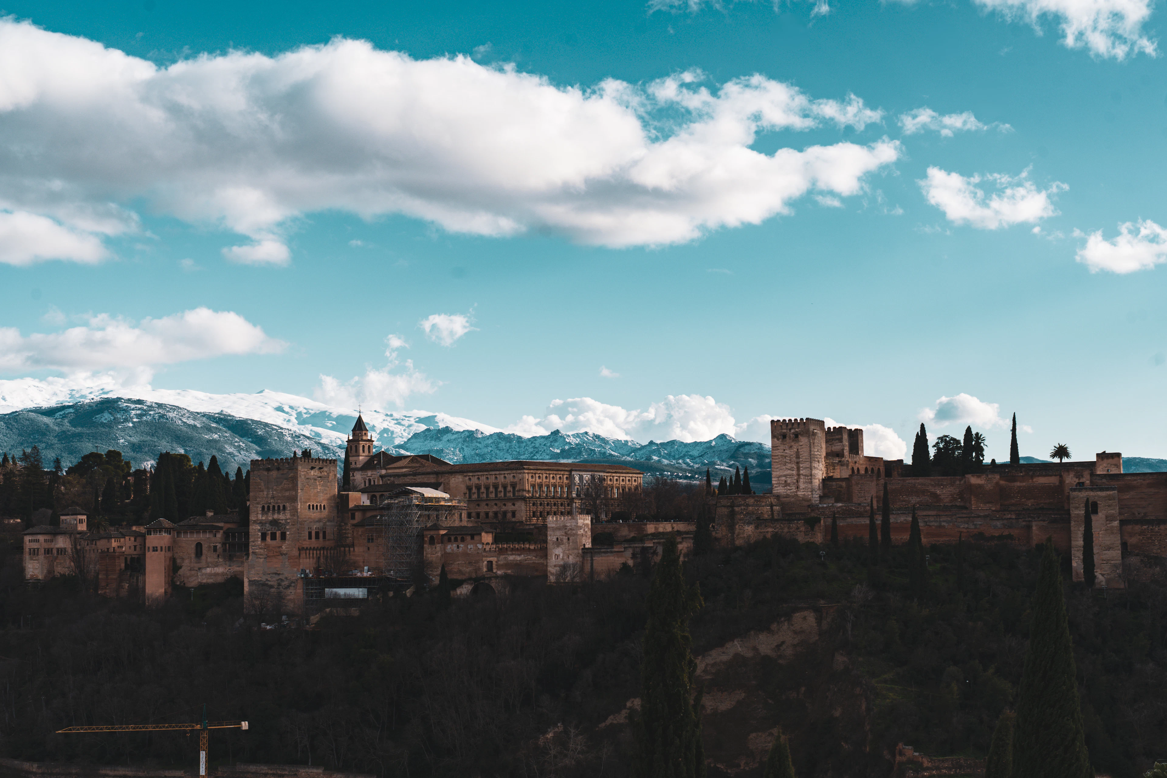 The Alhambra's walls stretch along a ridge with the snow-capped Sierra Nevada rising behind it.